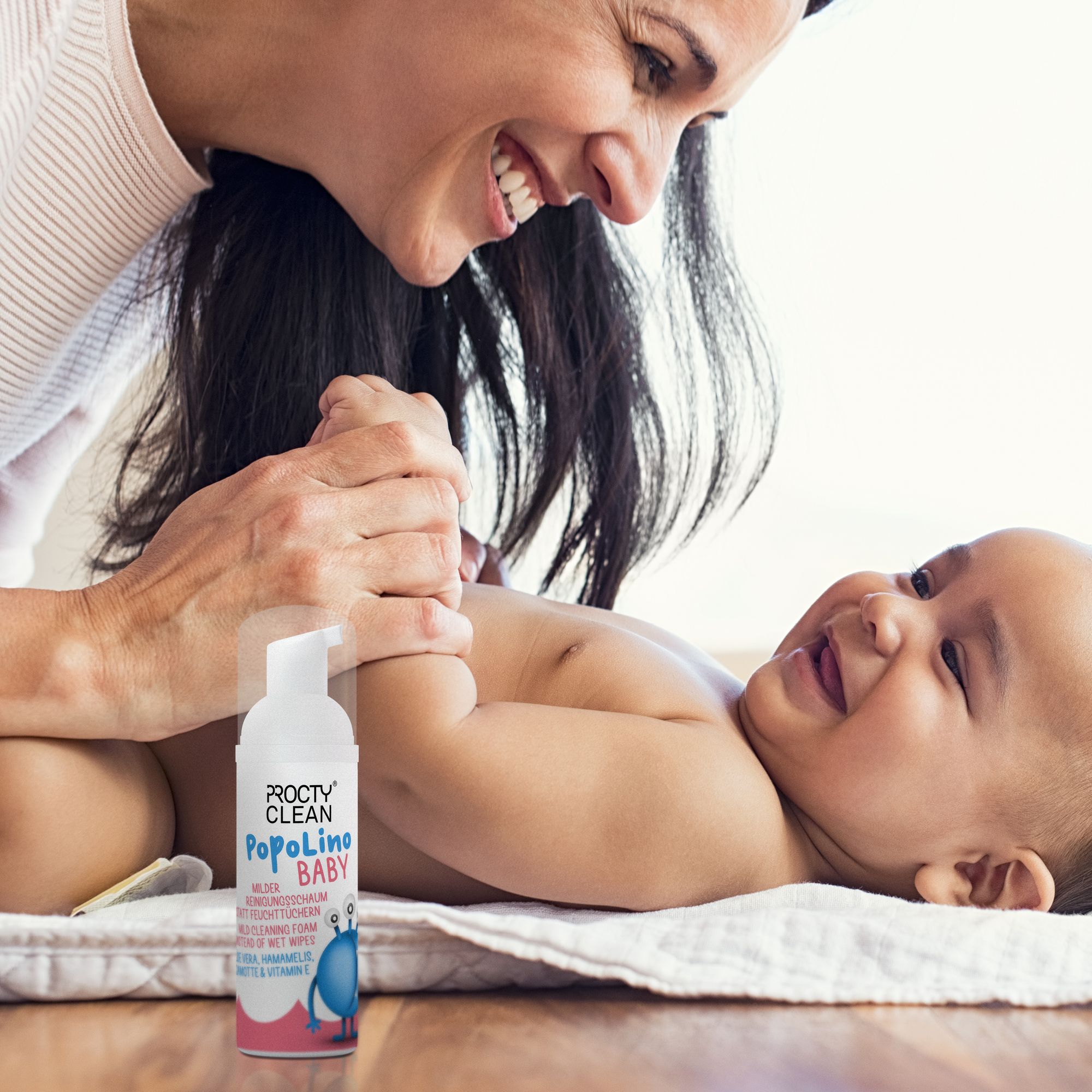 Frau und Baby. Baby liegt auf einer Unterlage. ProctyClean PopoLino Baby-Flasche im Bild.