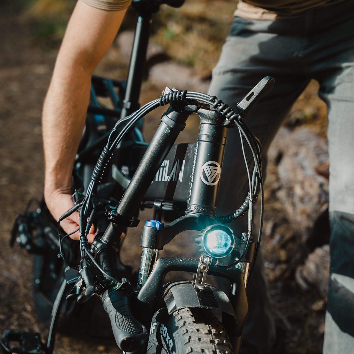 Nahaufnahme des Lenkers eines Vitilan V3 2.0 E-Bikes. Scheinwerfer, Logo und Details sichtbar. Person hält das Fahrrad.