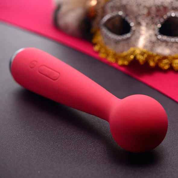 Roter Massage-Wand. Kugel am Ende, länglicher Griff mit Knöpfen. Auf rotem Hintergrund, Maske im Hintergrund.