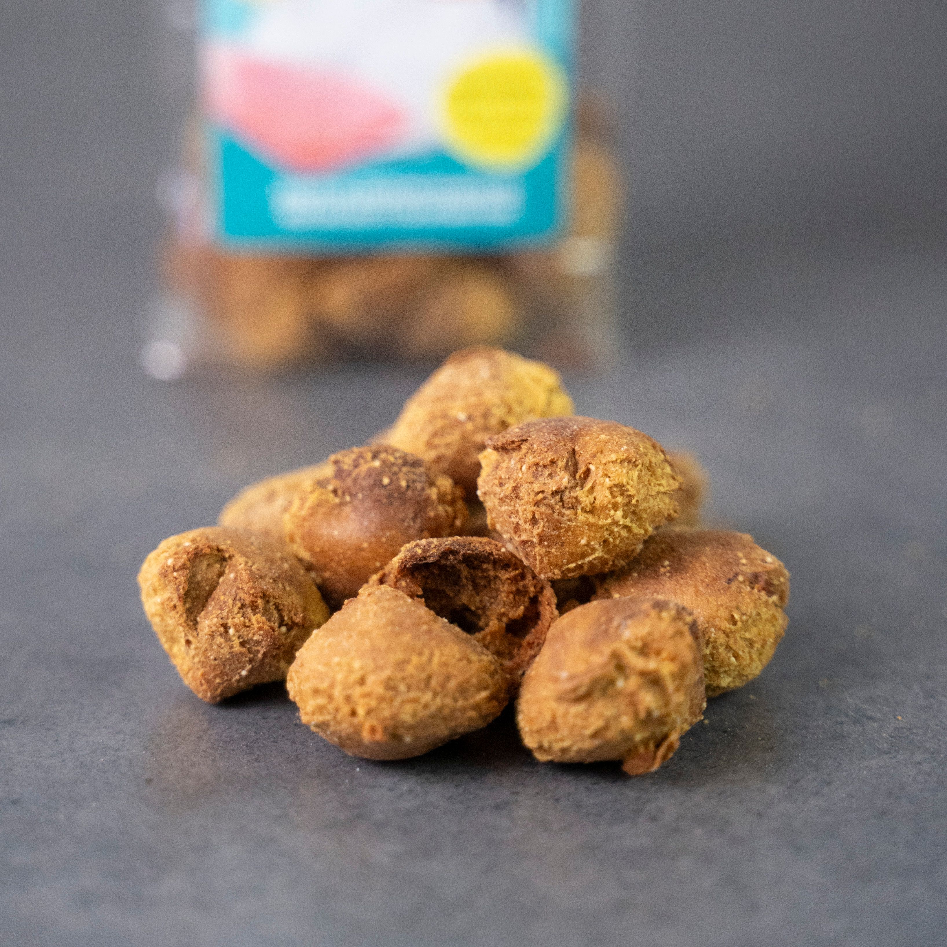 Haufen von runden, goldbraunen Hundesnacks. Einige Snacks sind aufgeschnitten. Im Hintergrund ist die Verpackung unscharf zu sehen.