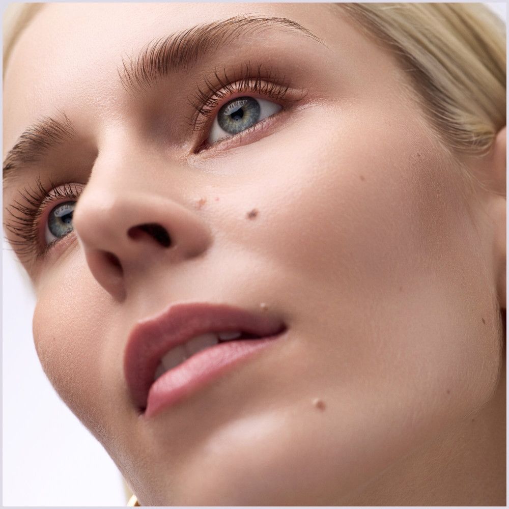 Nahaufnahme eines Gesichts. Augen mit getuschten Wimpern. Haut mit Sommersprossen. Blick nach oben.