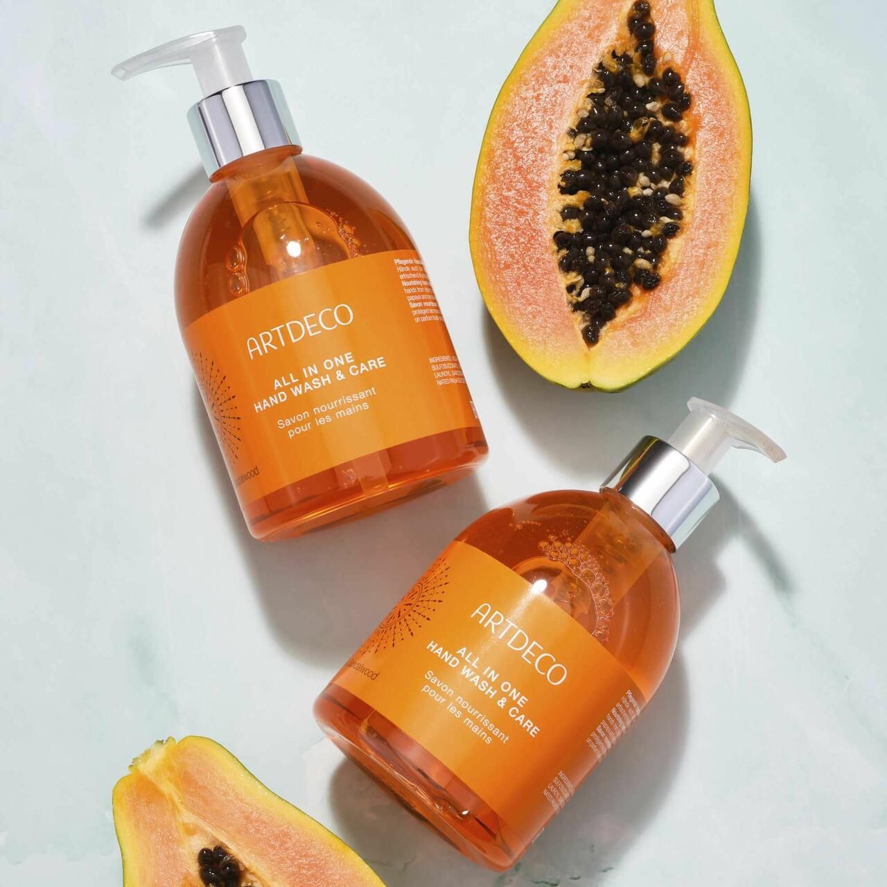 Zwei Flaschen Artdeco All in One Hand Wash & Care und zwei Papaya-Hälften. Aufschrift: All in One Hand Wash & Care.
