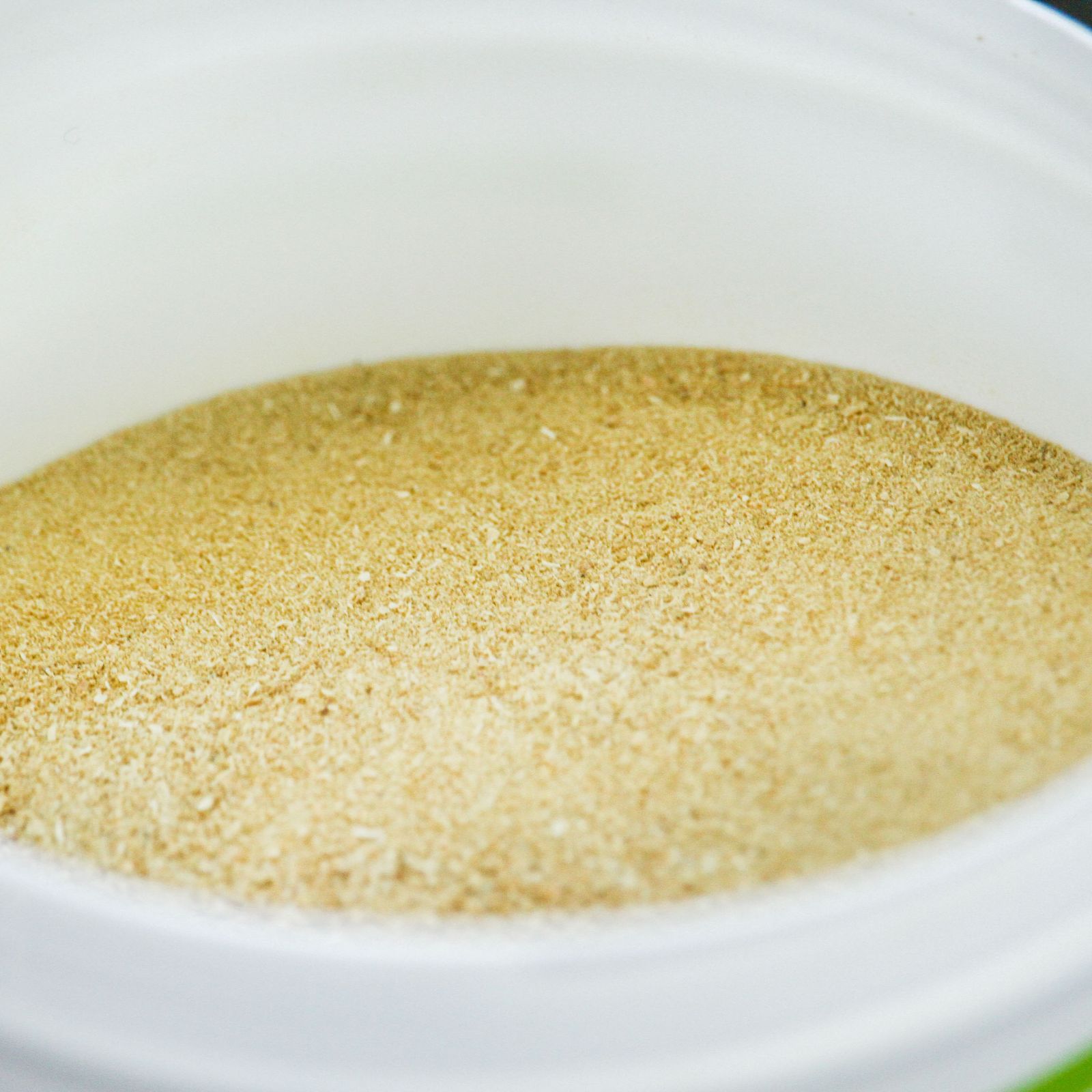 Nahaufnahme von Muschelpulver in einer weißen Schüssel. Das Pulver ist hellbraun und körnig.