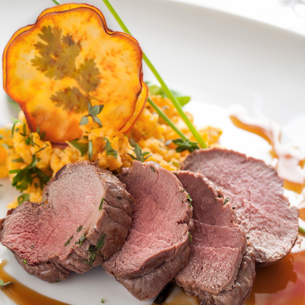 Teller mit Fleisch, Gemüse und Soße. Fleisch in Scheiben geschnitten, Gemüsechips und Kräuter. Weiße Platte.