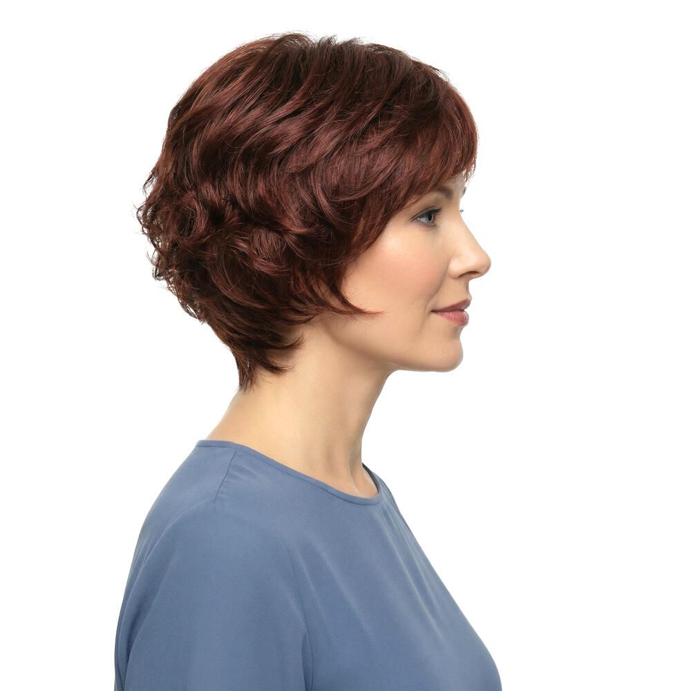 Profil einer Frau mit roter Perücke. Kurzer, gewellter Haarschnitt. Blauer Pullover. Seitenansicht.
