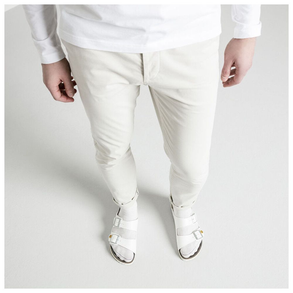 Draufsicht auf Person in beiger Hose und weißen Sandalen. Sandalen mit zwei Riemen, Marke Birkenstock.