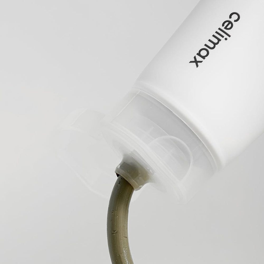 Nahaufnahme des Auslasses einer Tube, aus der eine graugrüne Tonmaske austritt.