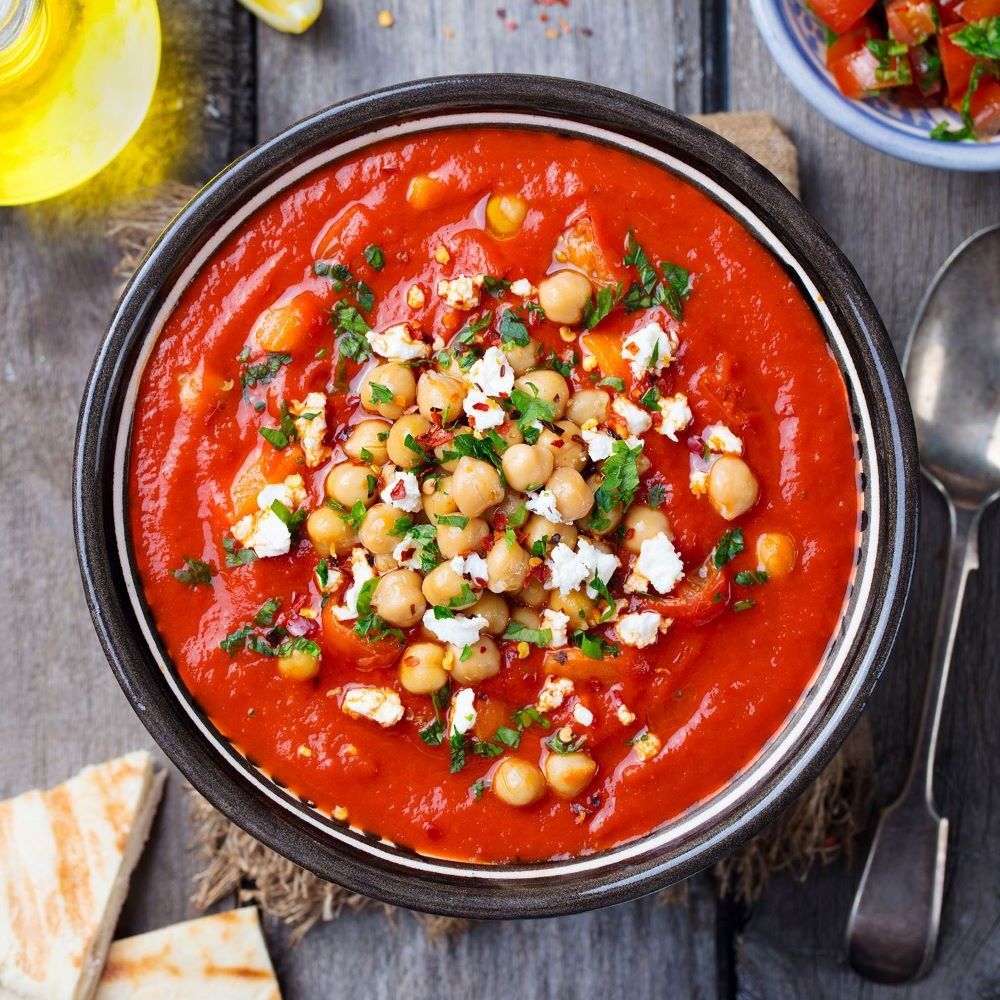 Rote Suppe in einer Schüssel. Kichererbsen, Käse und Kräuter auf der Suppe. Brotstücke am Rand.