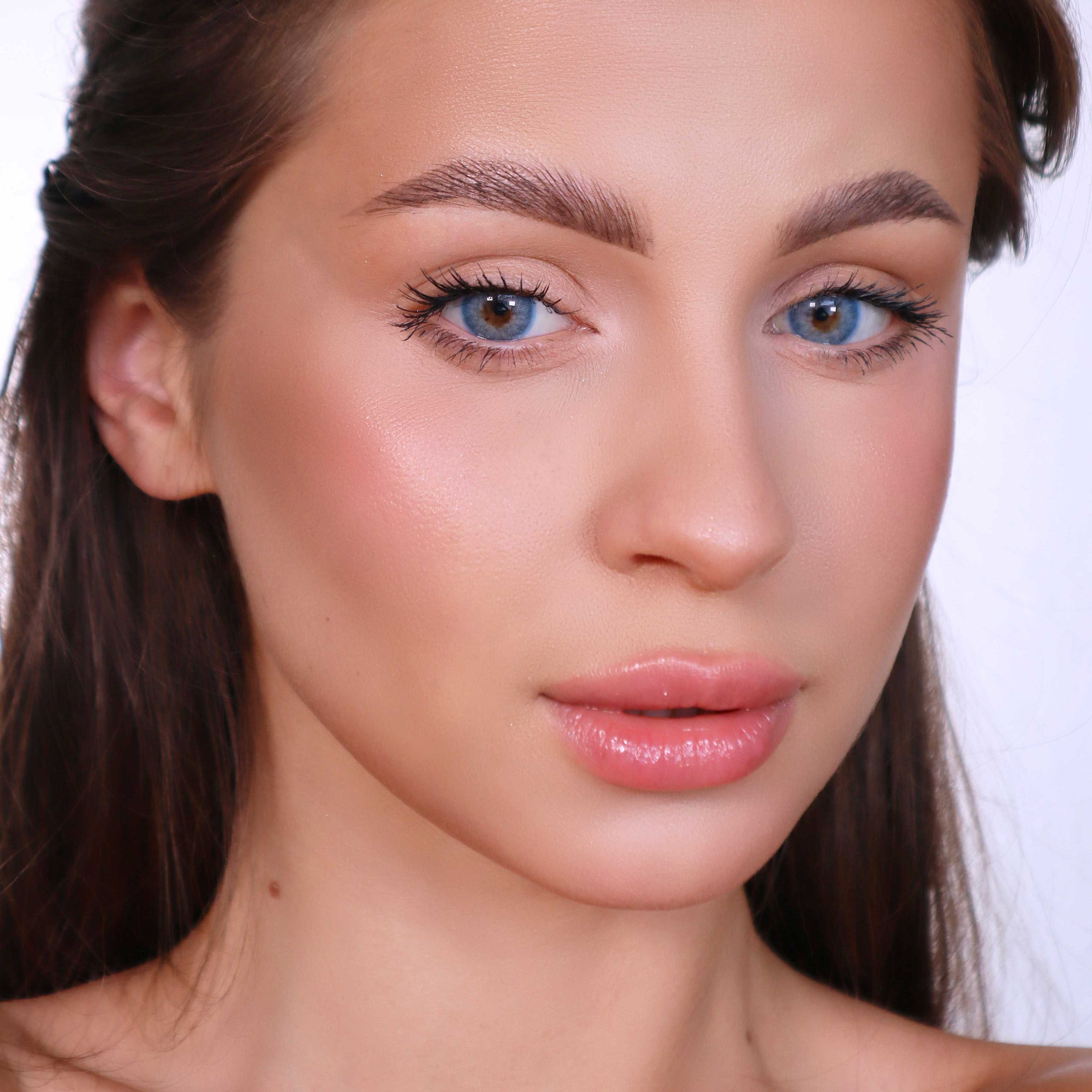 Porträt einer Frau mit blauen Augen. Sie blickt direkt in die Kamera. Hautton und Make-up sind deutlich sichtbar.