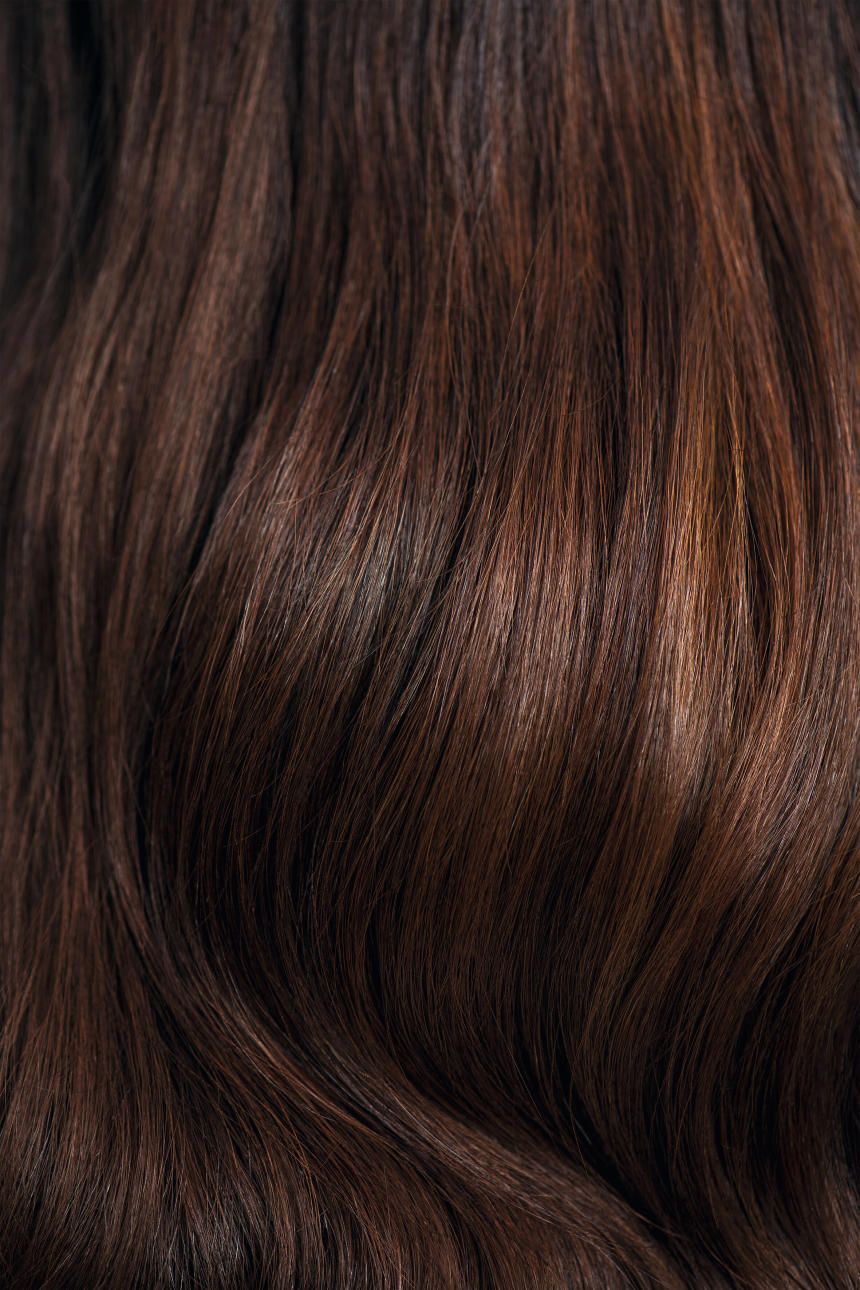 Nahaufnahme von braunem, welligem Haar. Die Haarsträhnen sind in verschiedenen Brauntönen gefärbt.