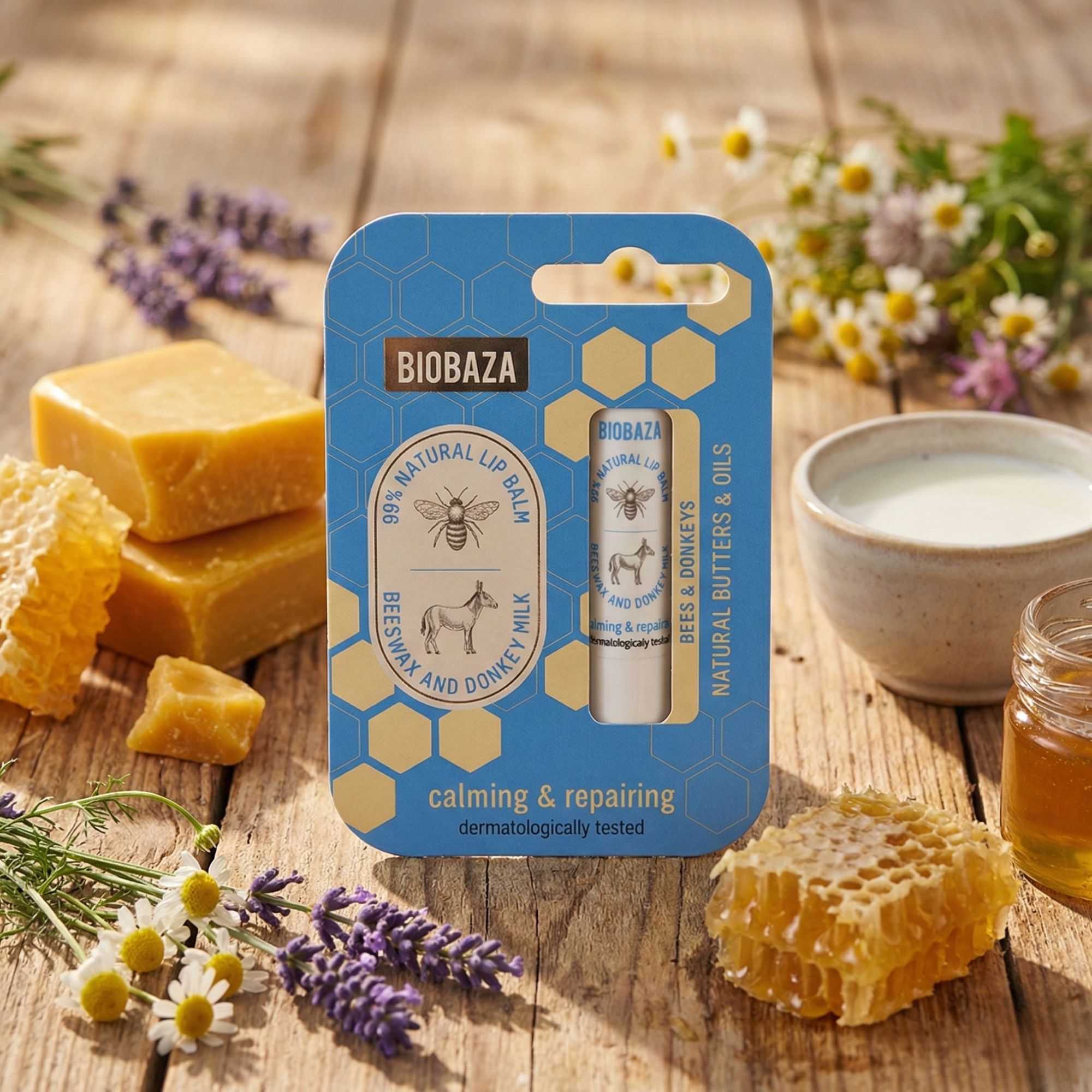 Produkt-Arrangement mit Lippenbalsam, Honigwaben, Milch, Honigglas und Blumen auf einem Holztisch.