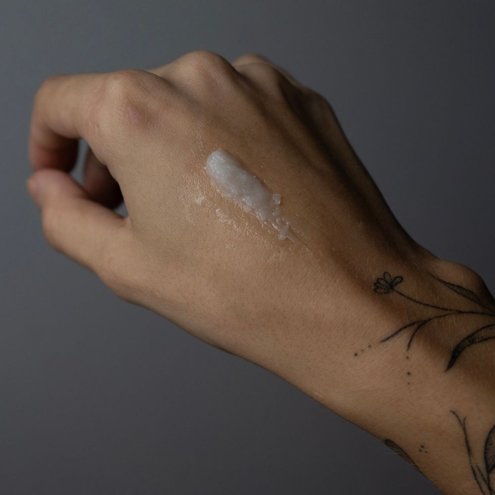Hand mit weißem Balsam. Tattoo-Details. Der Balsam ist auf der Haut verteilt.