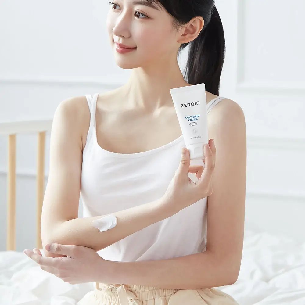Frau hält Tube ZEROID Soothing Cream. Creme auf Arm aufgetragen. Weiße Tanktop.