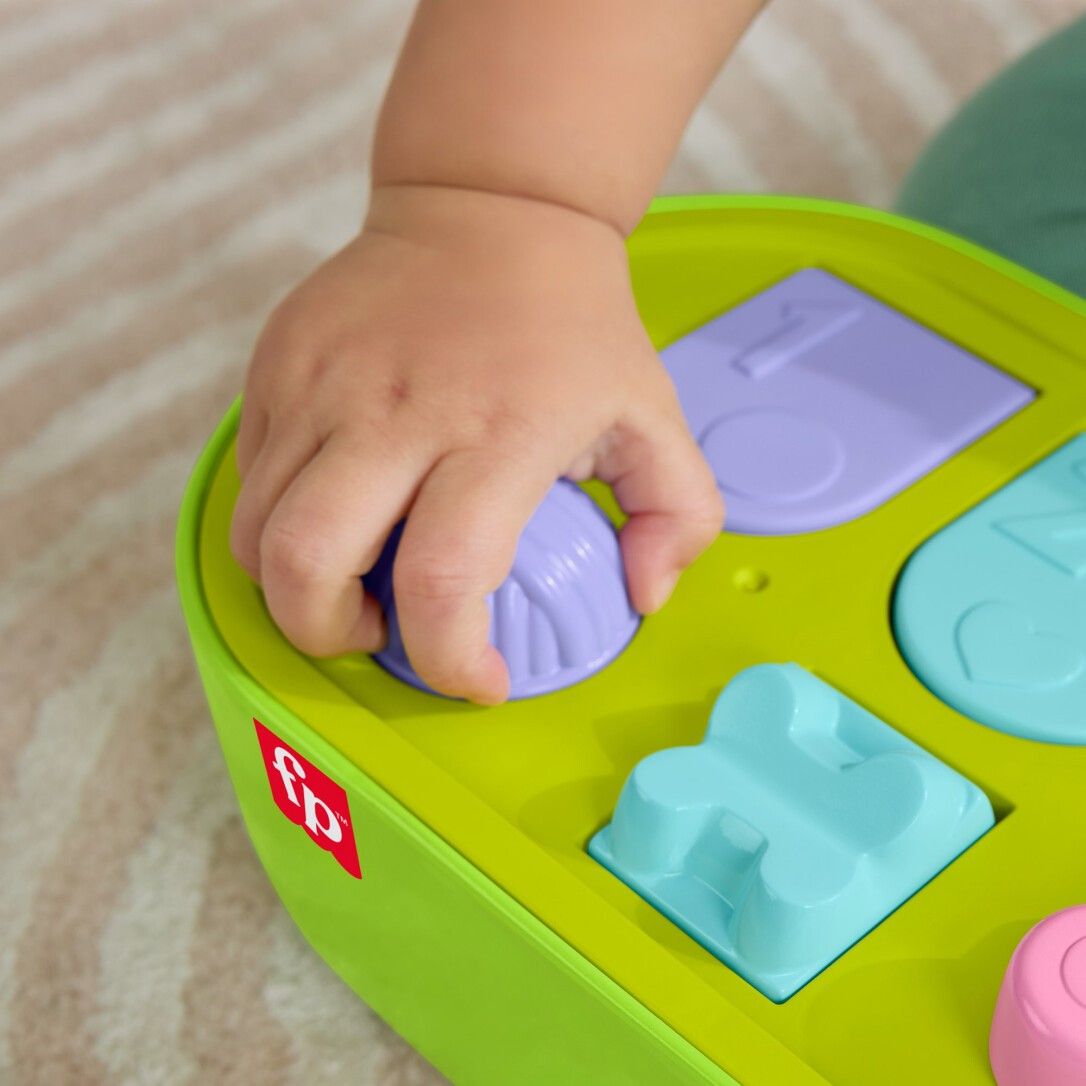 Nahaufnahme einer Hand, die einen lila Knopf drückt. Grünes Spielzeug mit bunten Knöpfen.