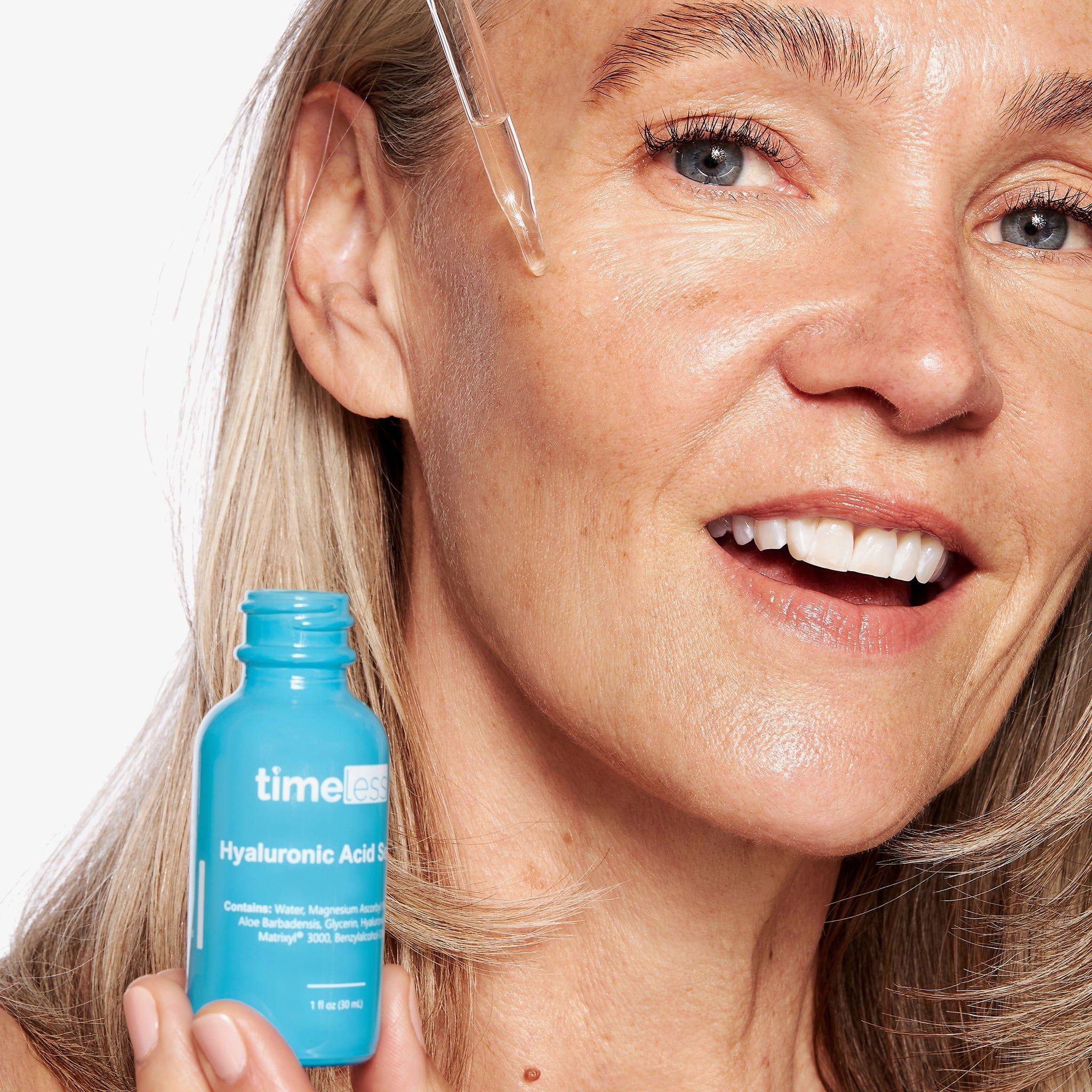 Frau mit Serumflasche. Sie hält die Flasche und trägt das Serum auf. Aufschrift: Timeless Hyaluronsäure Serum.