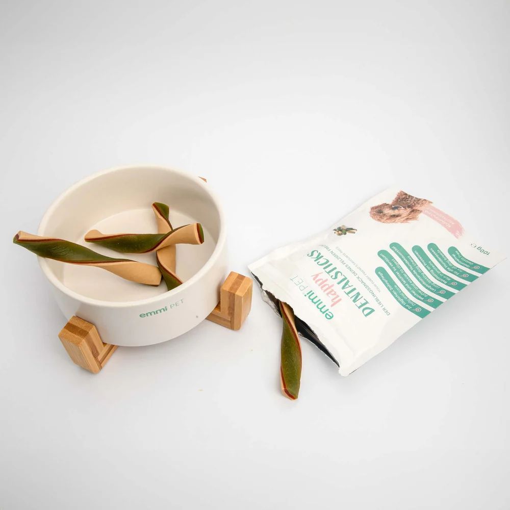 Beige Schale mit Holzfüßen, gefüllt mit grünen und beigen Dentalsticks. Daneben eine Packung Dentalsticks.