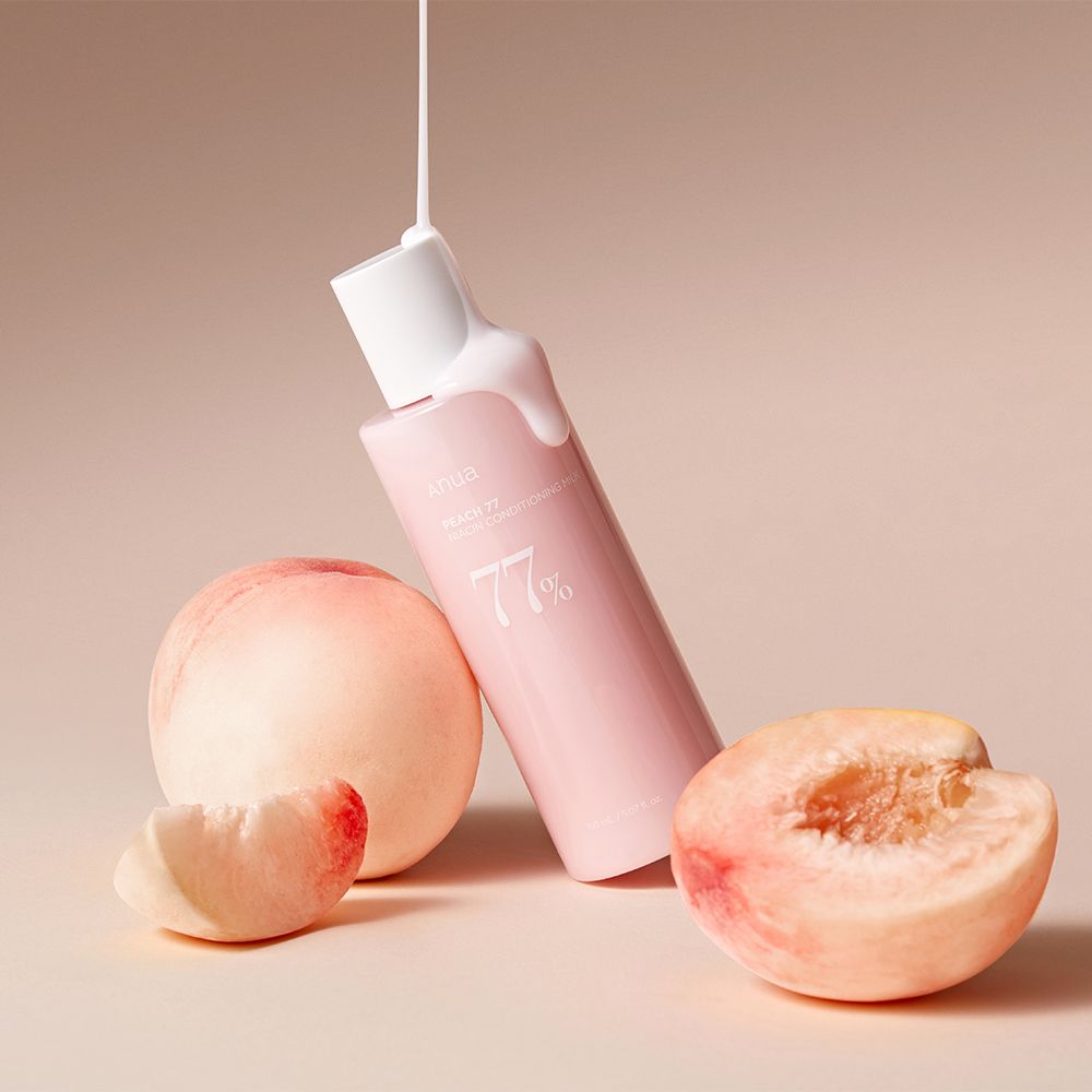 Anua Peach 77% Tonerflasche mit Schaum, umgeben von frischen Pfirsichen.
