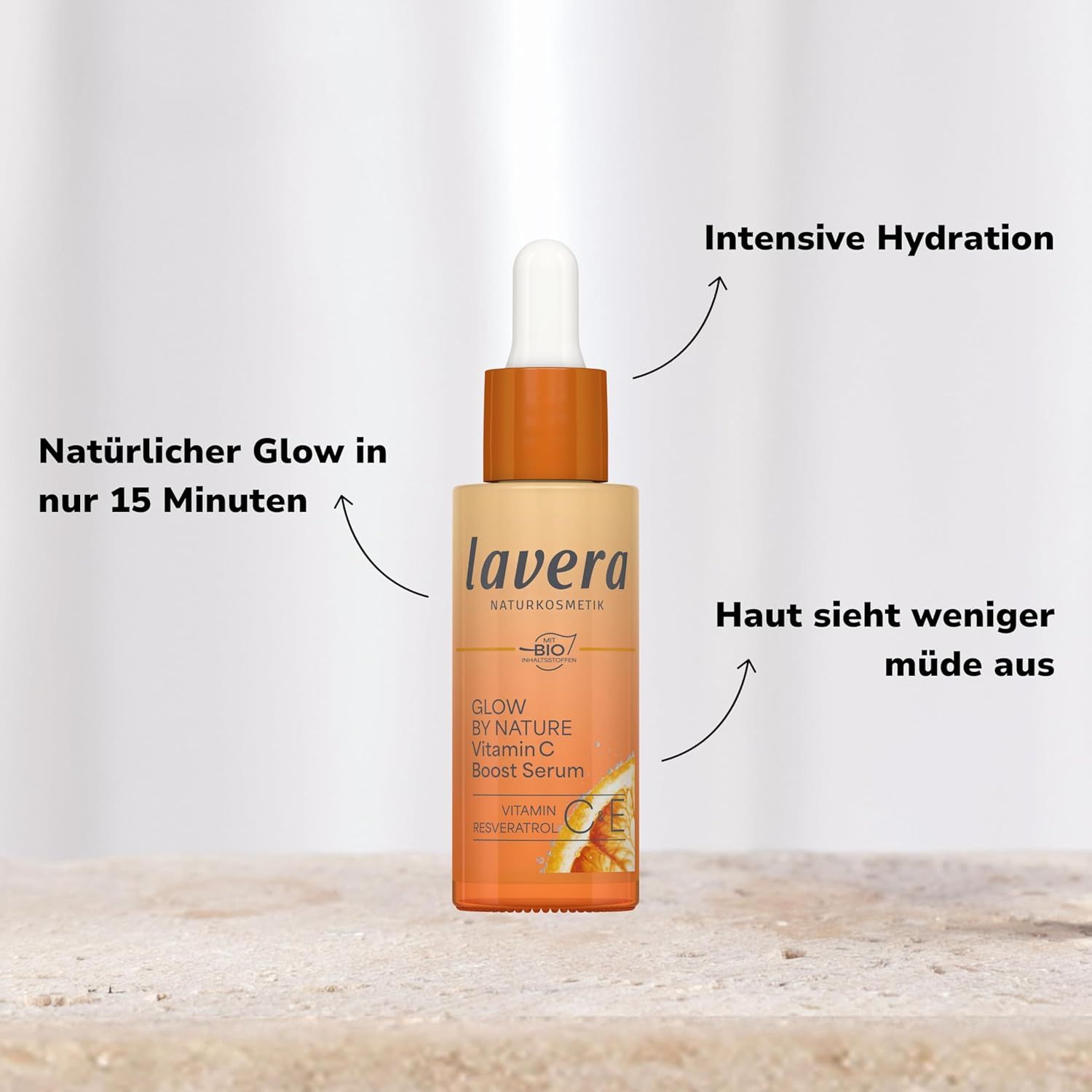 Serumflasche mit Text. Flasche mit orangefarbenem Deckel. Text: lavera, Glow By Nature Vitamin C Boost Serum. Pfeile zeigen auf Text.