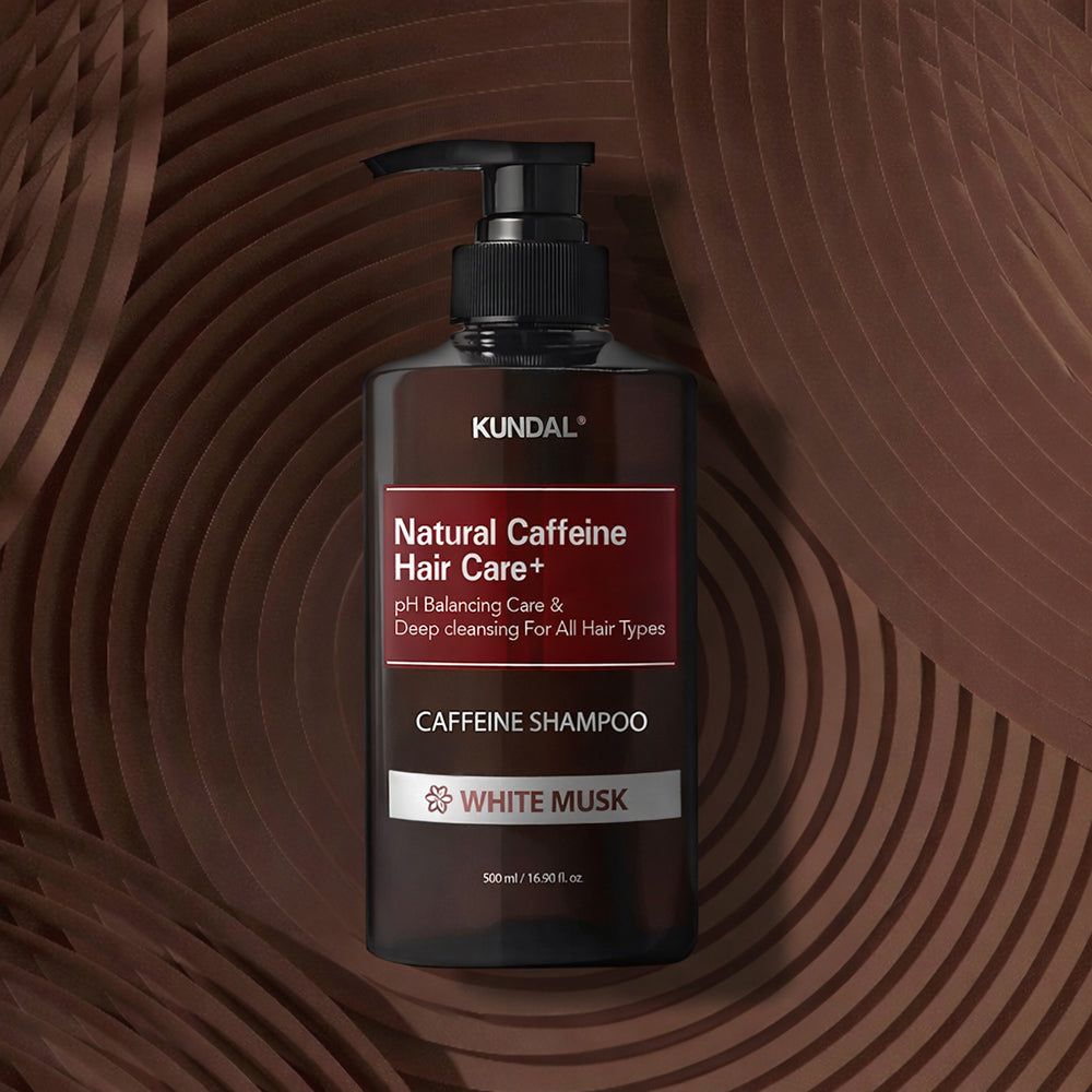 KUNDAL Natural Caffeine Hair Care+ Shampoo (White Musk) auf einem dekorativen braunen Hintergrund.