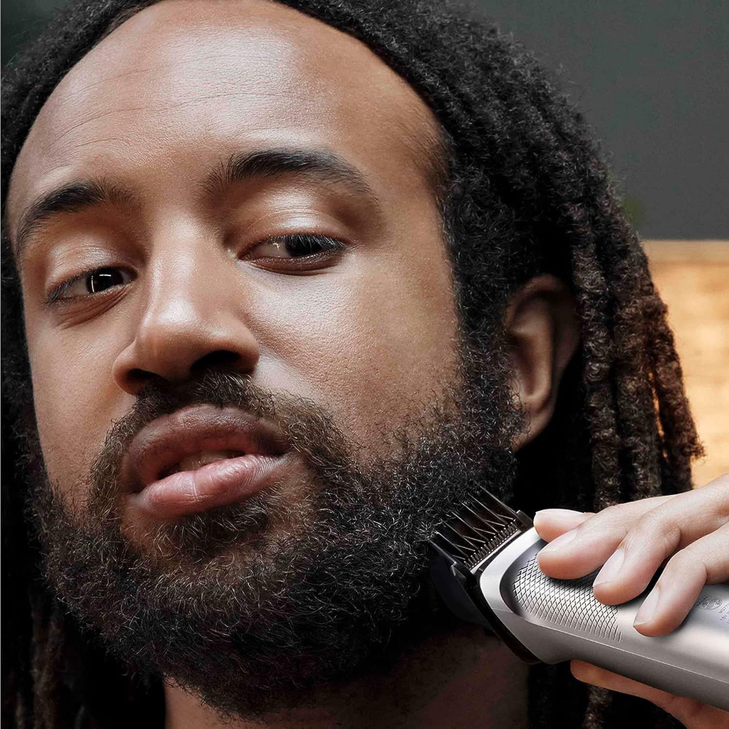 Person schneidet Bart mit Philips Multigroom Trimmer. Schwarzer Bart, Trimmer mit Aufsatz. Nahaufnahme.