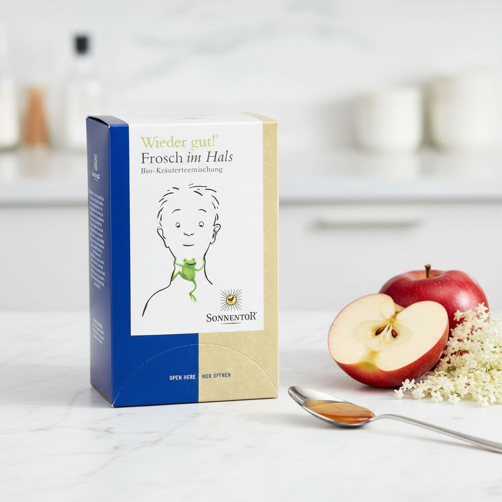 SonnentoR® Frosch im Hals® Tee-Verpackung auf einem Küchentisch mit Apfel und Tee.