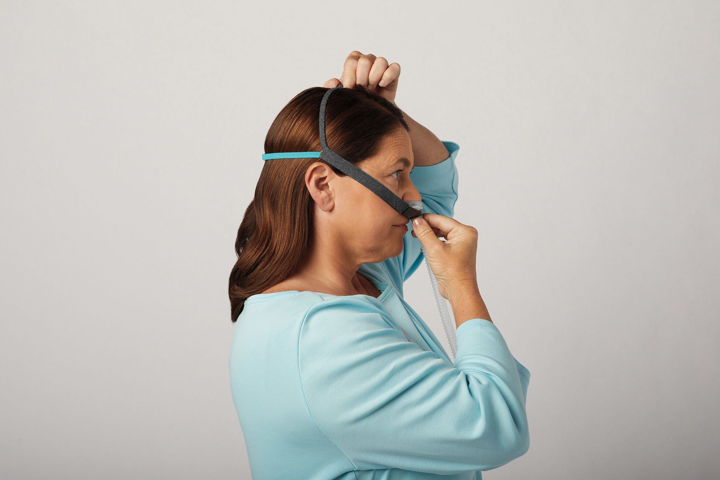 Frau setzt CPAP-Nasenmaske mit Kopfteil auf.