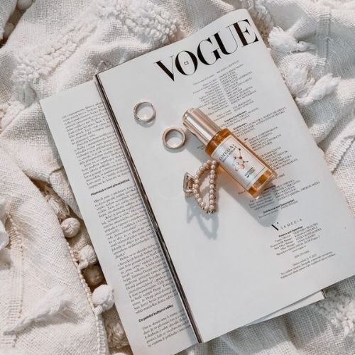 Serumflasche auf Vogue-Magazin. Goldfarbener Deckel. Neben Schmuck: Ringe und Armband. Text auf Etikett nicht lesbar.
