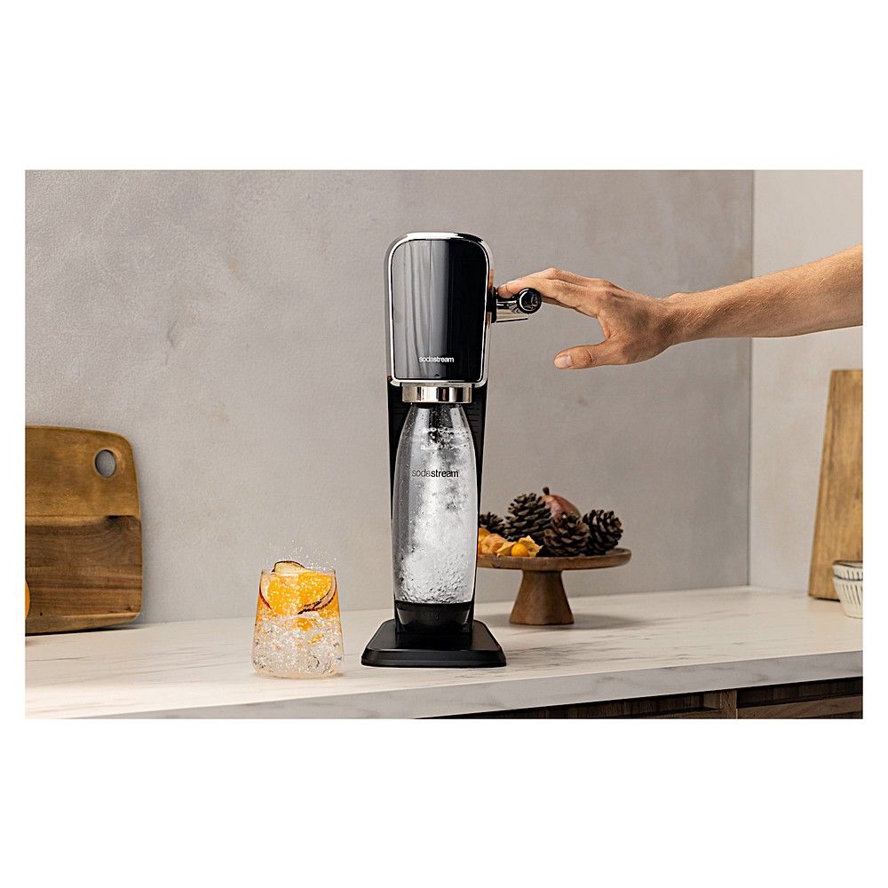 Hand bedient SodaStream Art Wassersprudler neben einem Glas.