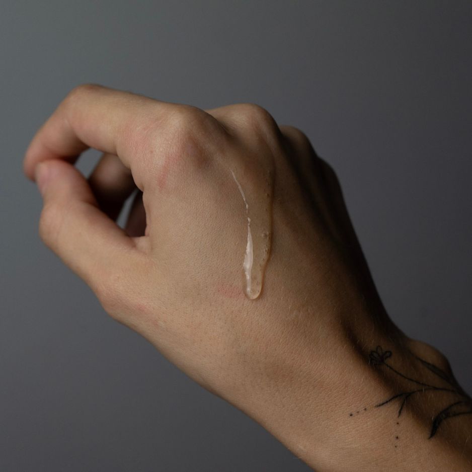 Hand mit durchsichtigem Gel. Das Gel tropft auf die Haut. Hintergrund grau.