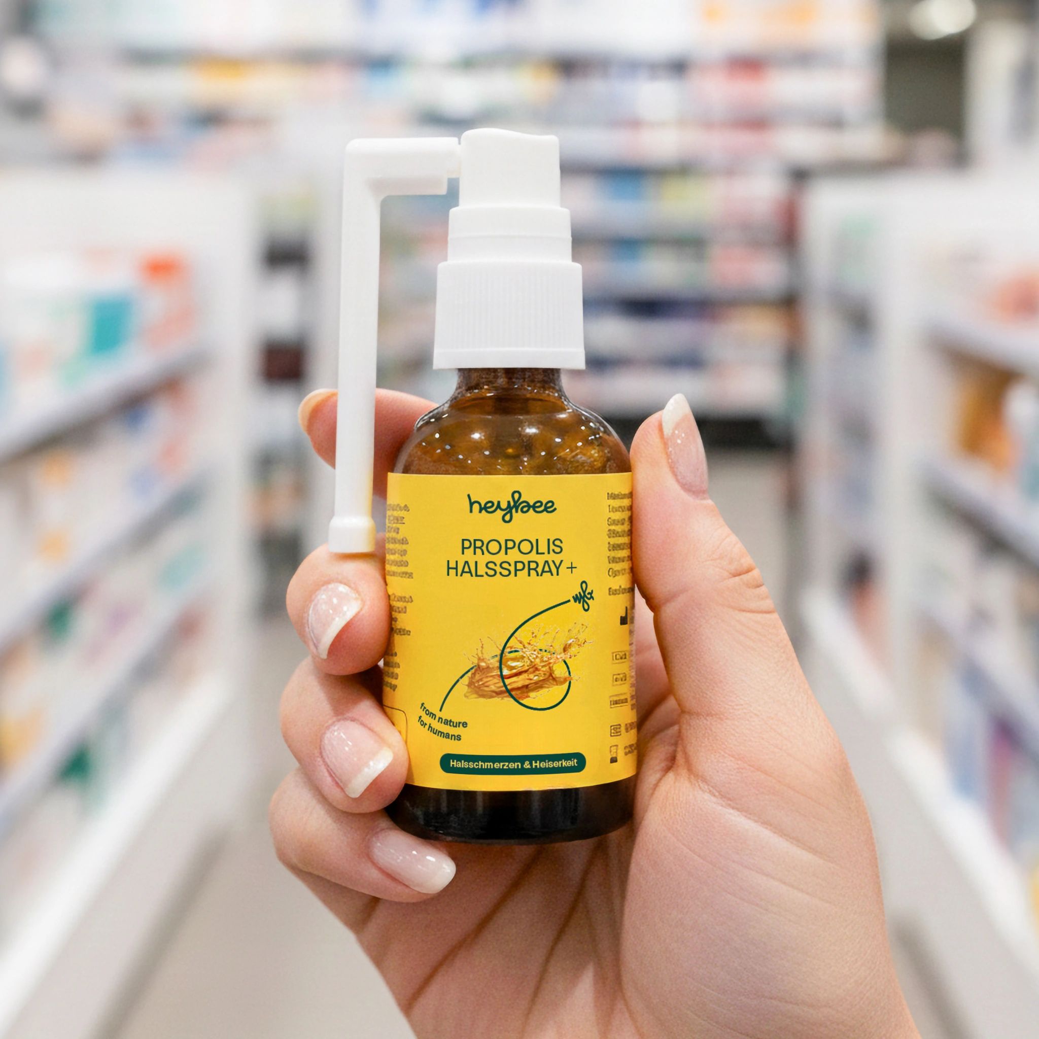 Hand hält Heybee Propolis Halsspray+ Flasche. Braune Flasche mit weißem Sprühkopf. In einer Apotheke.