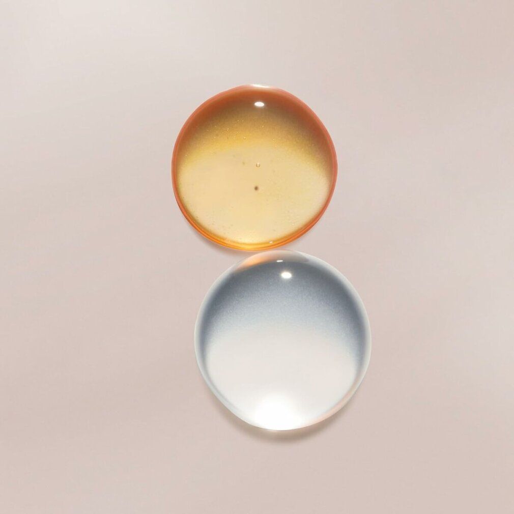 Zwei Tropfen Flüssigkeit, eine orange und eine klar, von Lancaster Sun Beauty Sonnenwasser.