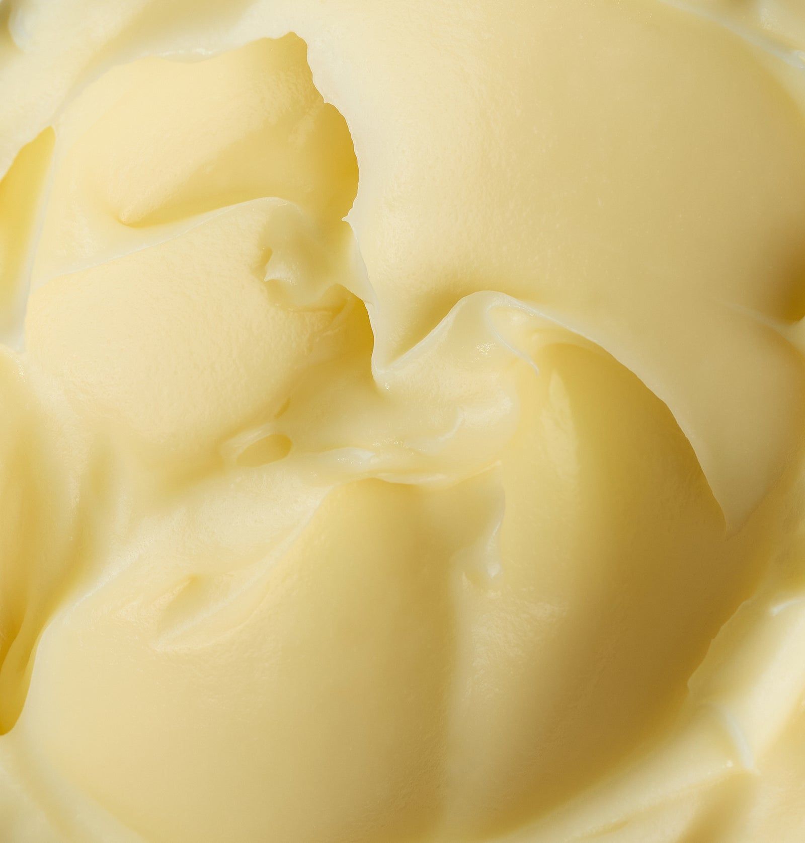 Nahaufnahme von cremiger, gelber Creme. Textur mit gewirbelten Formen.