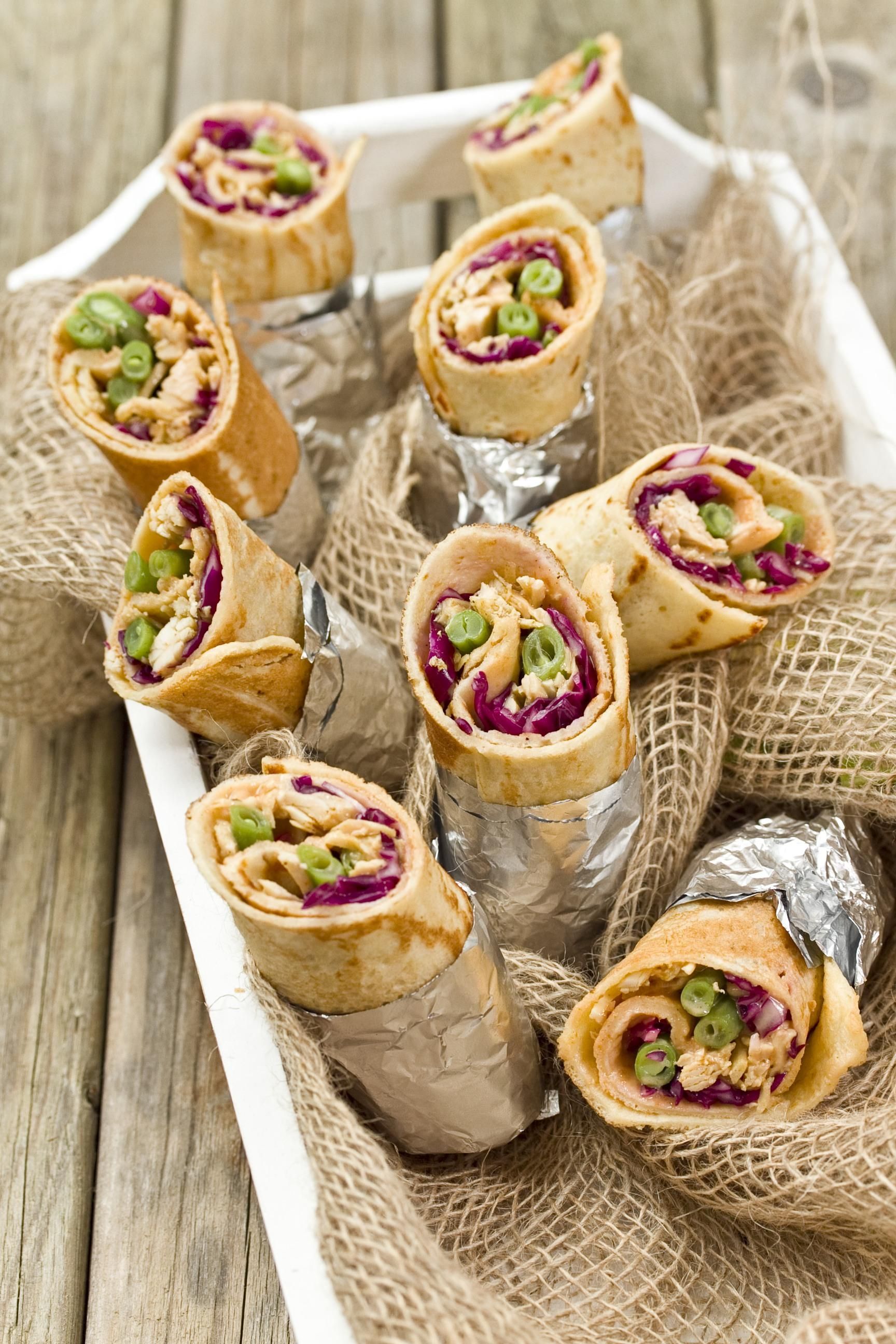 Serviertablett mit gerollten Wraps. Füllung aus Gemüse und Fleisch, in Folie gewickelt. Auf Leinen gelegt.