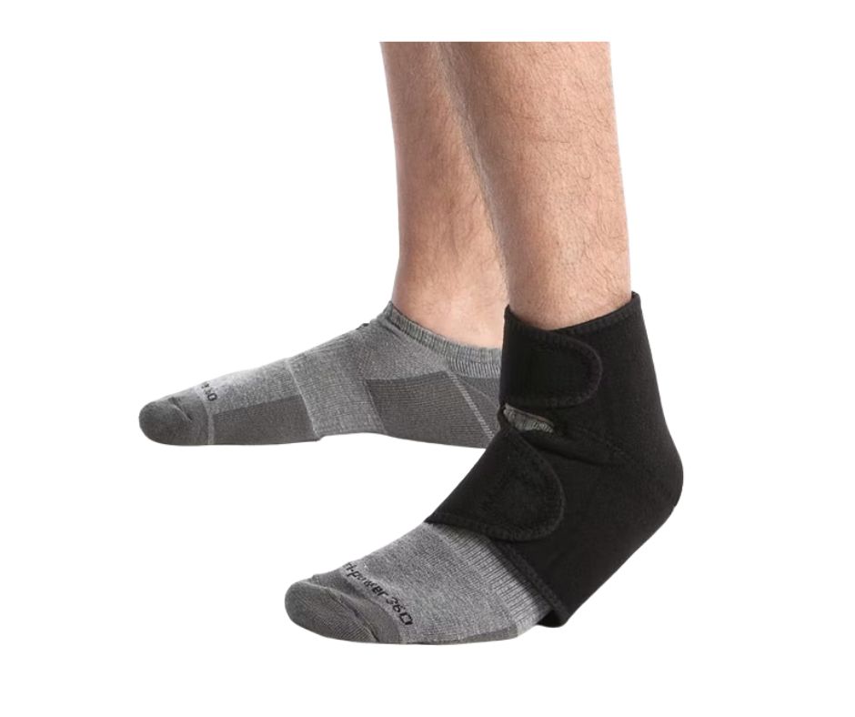Schwarze Fußgelenkbandage mit Klettverschlüssen, am Fuß getragen. Graue Socken. Nahaufnahme.