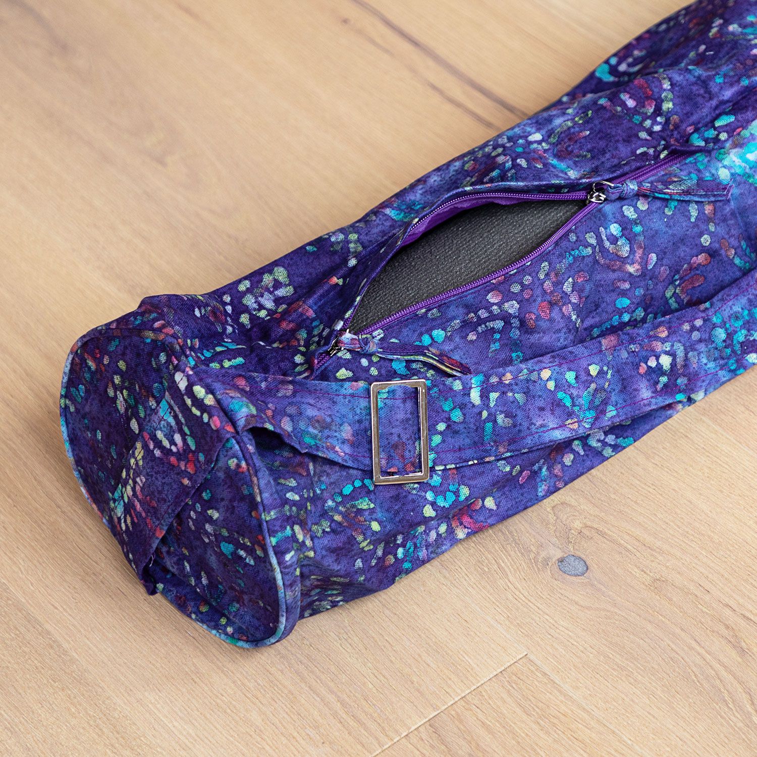 Sac de yoga ouvert, sur bois. Tissu lila à motifs colorés. Intérieur visible. Avec fermeture éclair et boucle.
