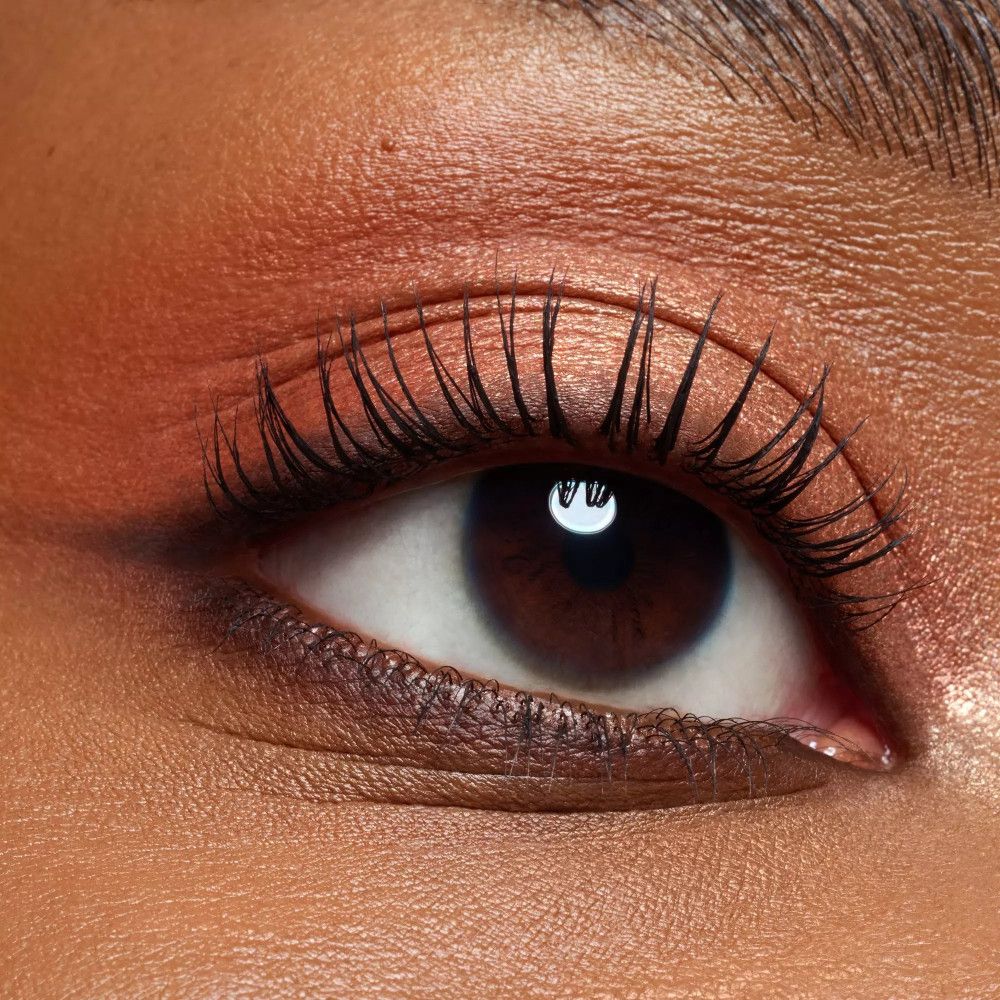 Nahaufnahme eines Auges mit Lidschatten. Farben: Orange und Braun. Wimpern getuscht. Hautton: dunkel.