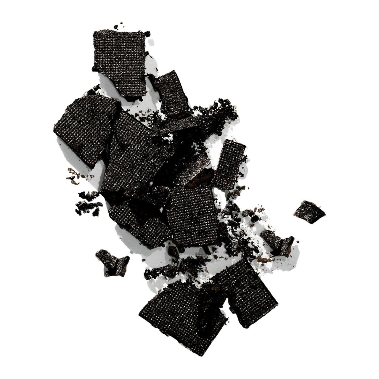 Zerkleinerte schwarze Color Wow Root Cover Up-Produktstücke. Gezeigt auf weißem Hintergrund. Verschiedene Formen und Größen.