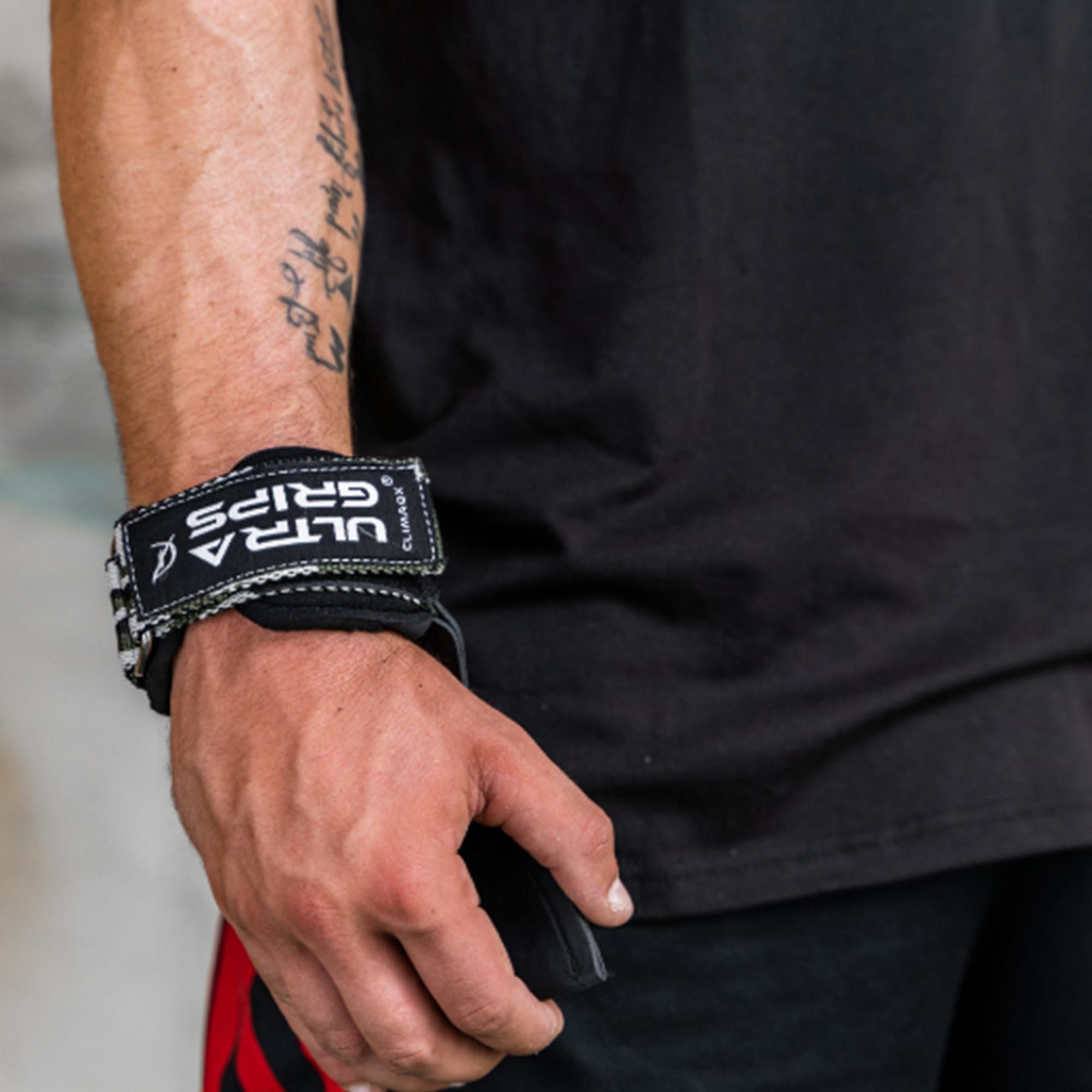 Handgelenk mit CLIMAQX Ultra-Grip. Schwarzes Leder, Text: ULTRA GRIPS. Person trägt schwarzes T-Shirt.