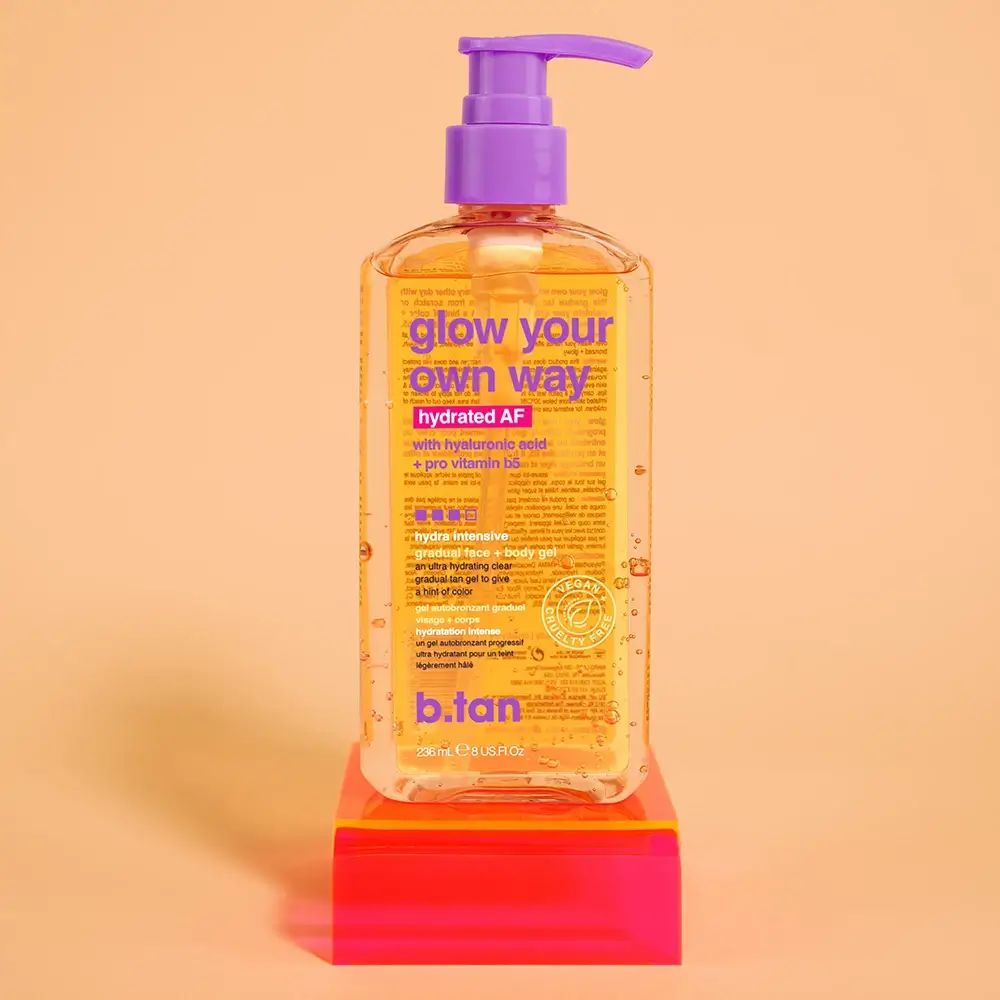 Transparente Flasche mit orangefarbenem Etikett. Aufschrift: glow your own way, hydrated AF, b.tan. Mit Pumpverschluss. Auf rotem Podest.