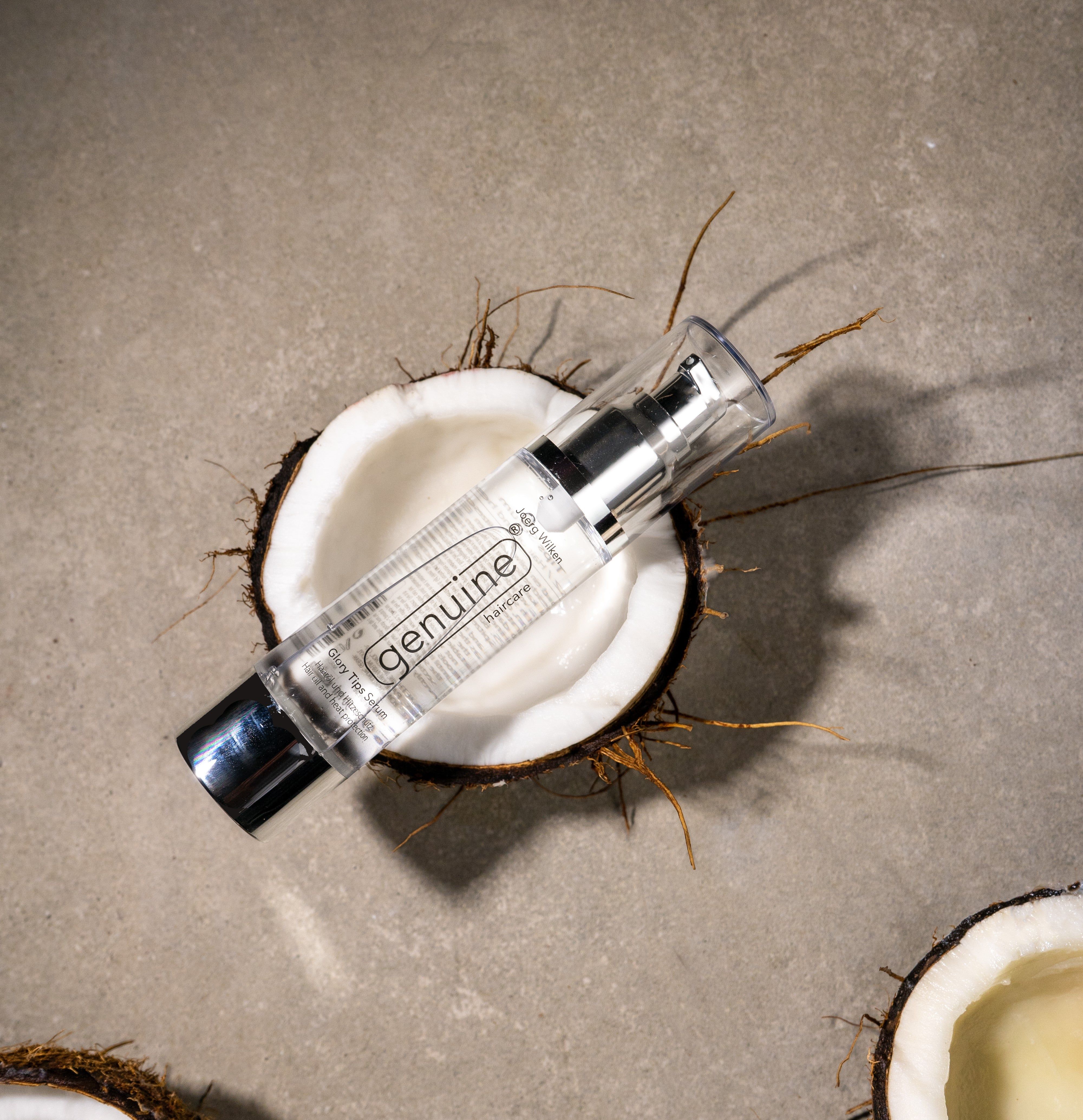 Klarer Serum-Flakon mit silberner Pumpe, auf Kokosnuss platziert. Aufschrift: genuine haircare.