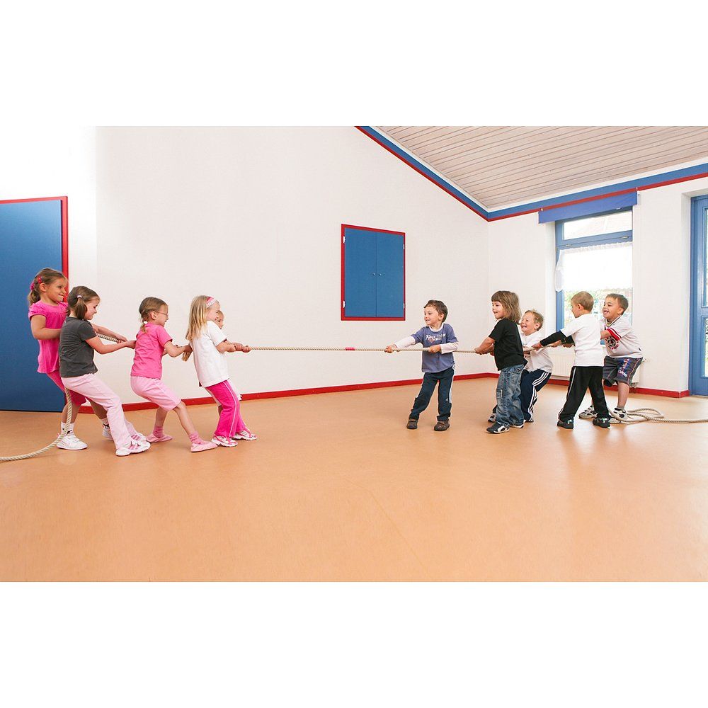 Kinder ziehen an einem Seil. Mehrere Kindergruppen ziehen an den Enden. Innenraum mit Holzboden und blauen Türen.