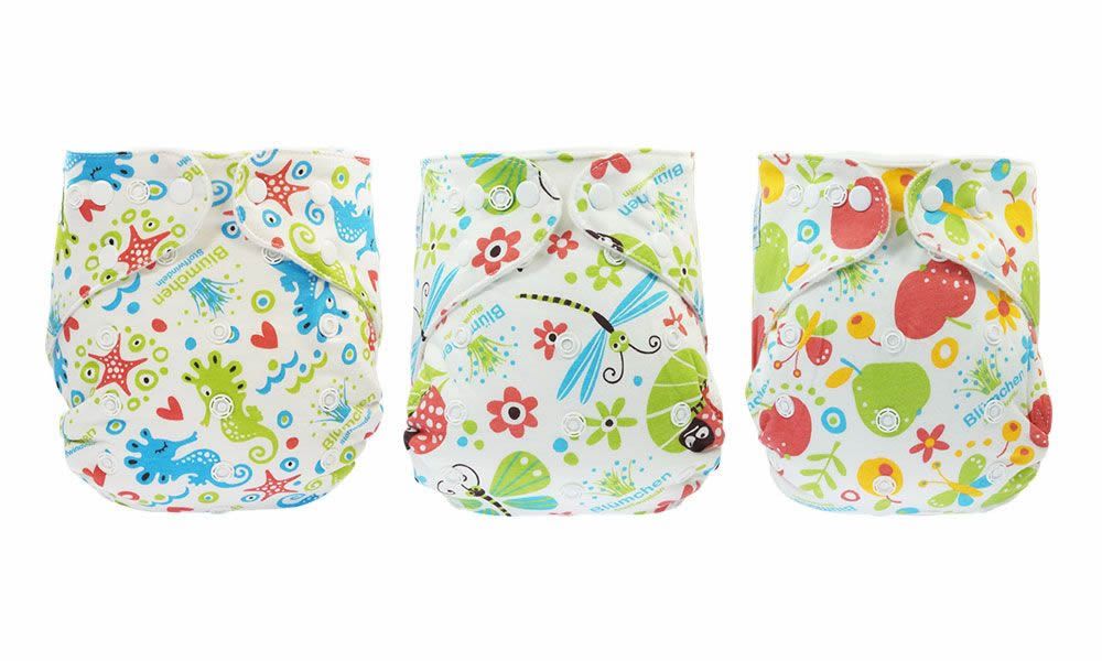 Drei Stoffwindeln nebeneinander. Unterschiedliche Muster: Seesterne, Libellen, Früchte. Weiße Druckknöpfe. Label mit Logo. Mehrfarbiges Design.