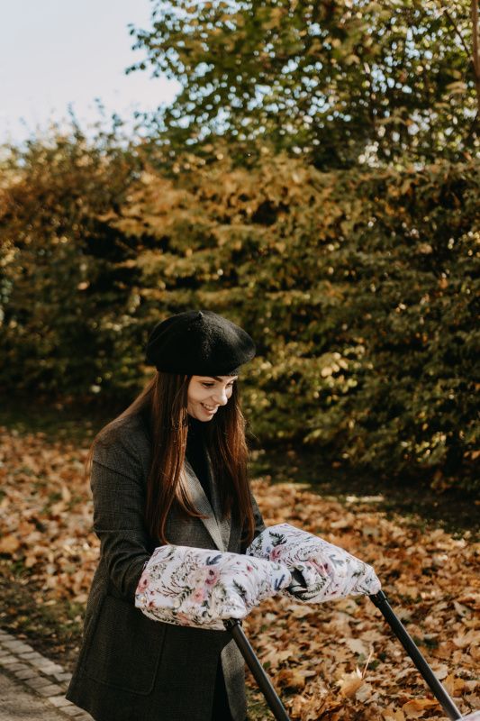 Frau mit schwarzem Barett schiebt Kinderwagen mit floralen Griffschützern.