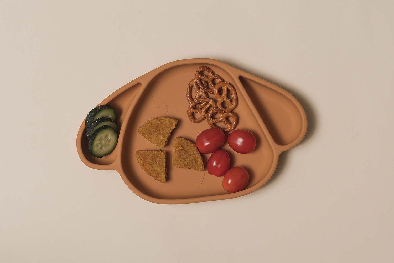 Hundeform-Teller mit Gemüse und Snacks. Gurkenscheiben, Brezeln, Tomaten und mehr.