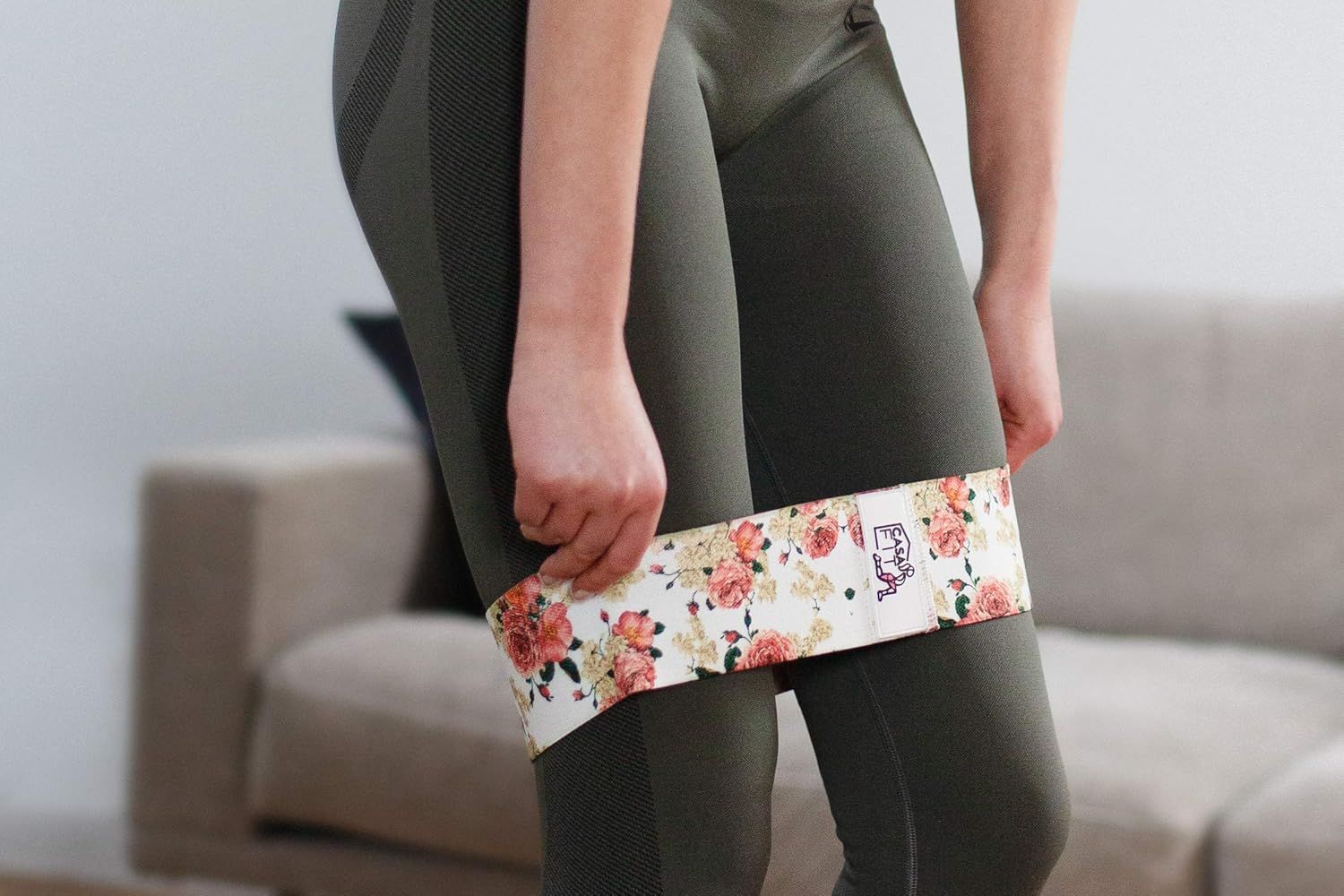 Person mit floralem Hüftband um die Oberschenkel. Hält das Band mit der Hand. Trägt grüne Leggings.