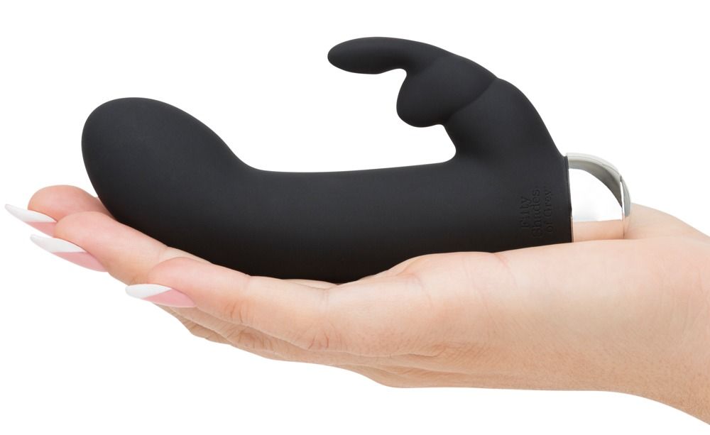 Schwarzer Rabbit-Vibrator in einer Hand gehalten. Mit zwei Vorsprüngen, einem für die Klitoris und einem für die vaginale Stimulation. Silberner Sockel.