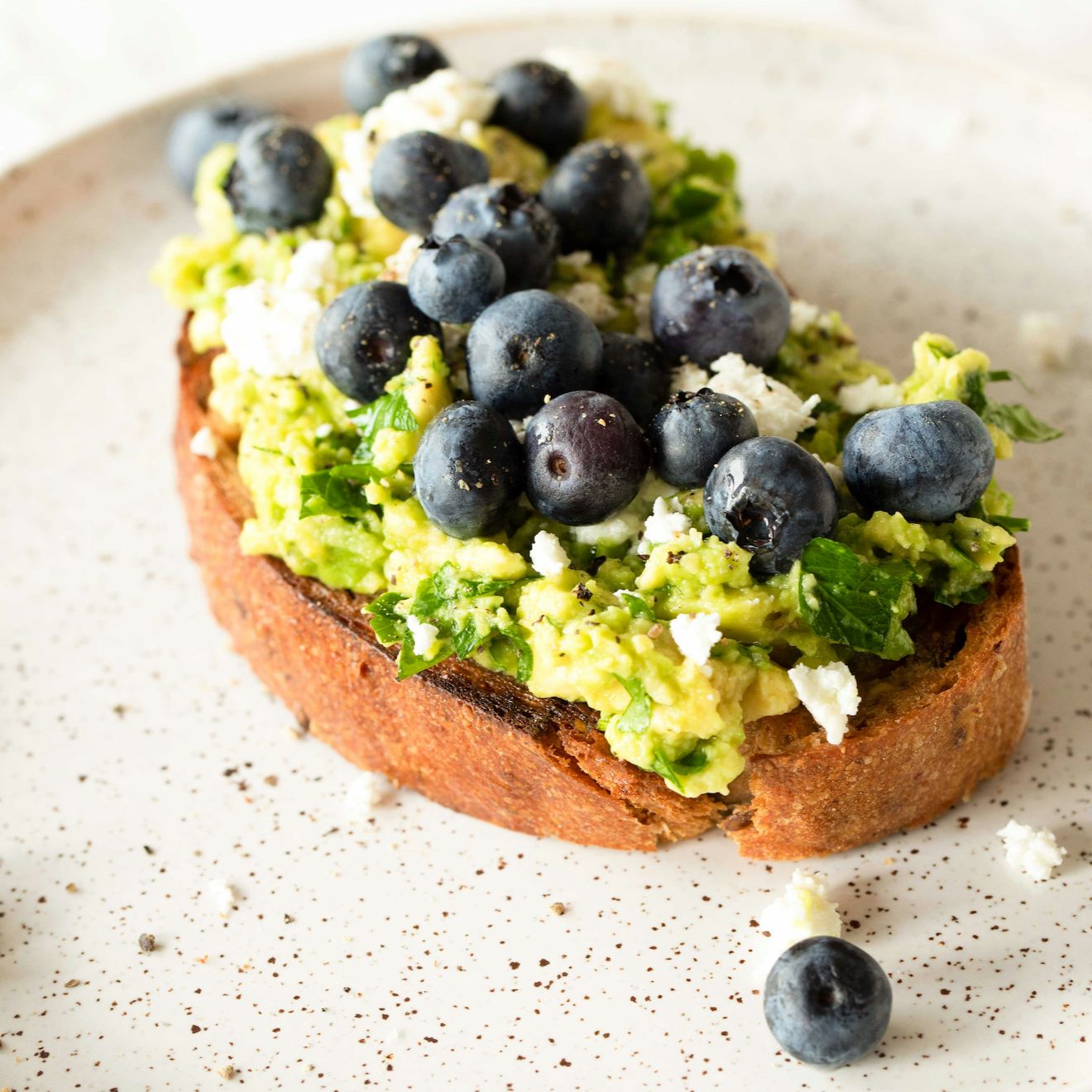 Geröstetes Brot mit Avocado, Blaubeeren und Käse auf einem Teller. Nahaufnahme.