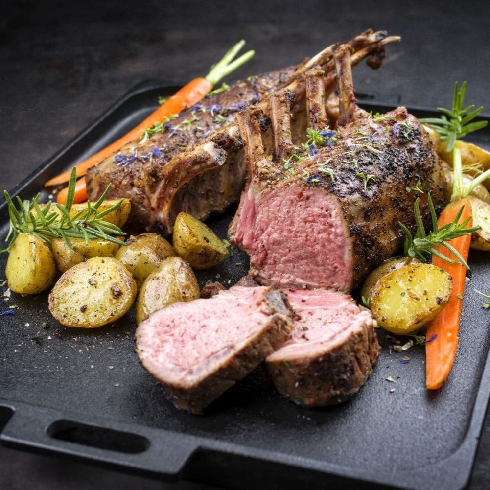 Gebratenes Lammkarree auf schwarzem Tablett. Mit Kartoffeln, Karotten und Rosmarin garniert. Fleisch geschnitten.