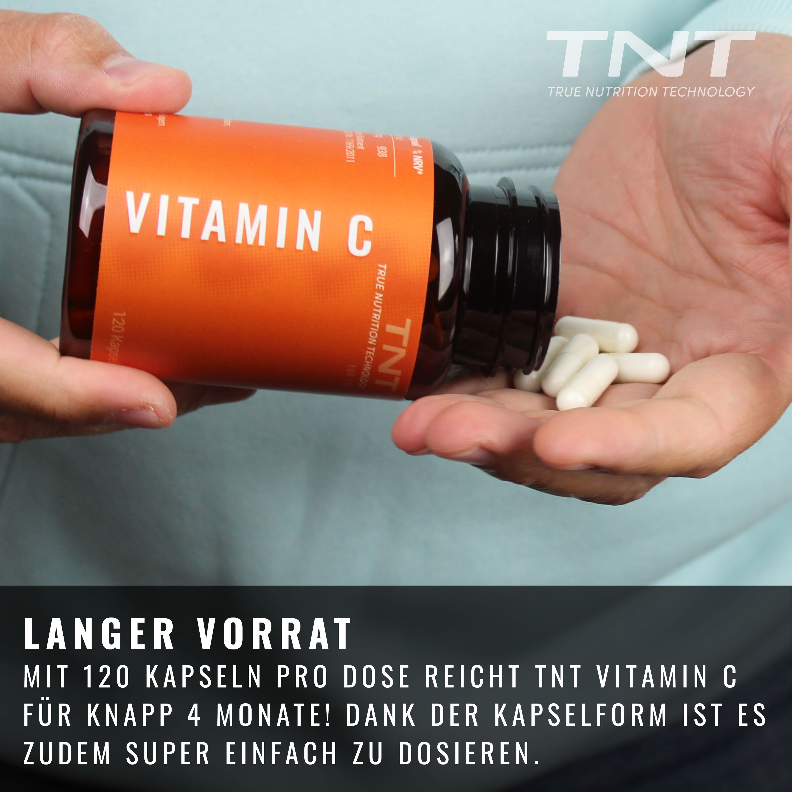 Hand hält TNT Vitamin C-Flasche. Orangefarbenes Etikett mit "Vitamin C" und "120 Kapseln". Einige Kapseln in der Hand.
