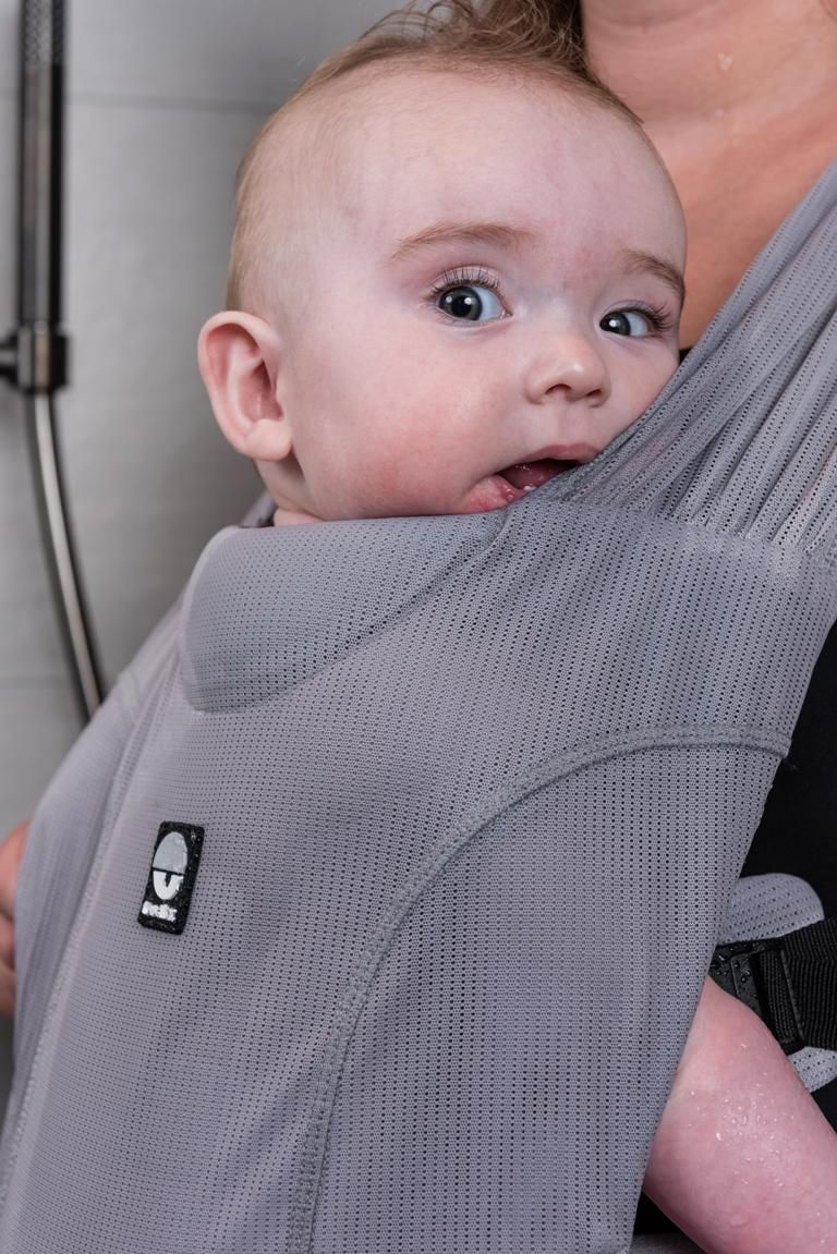 Nahaufnahme des Babys in der grauen Babytrage. Dooky-Logo sichtbar.